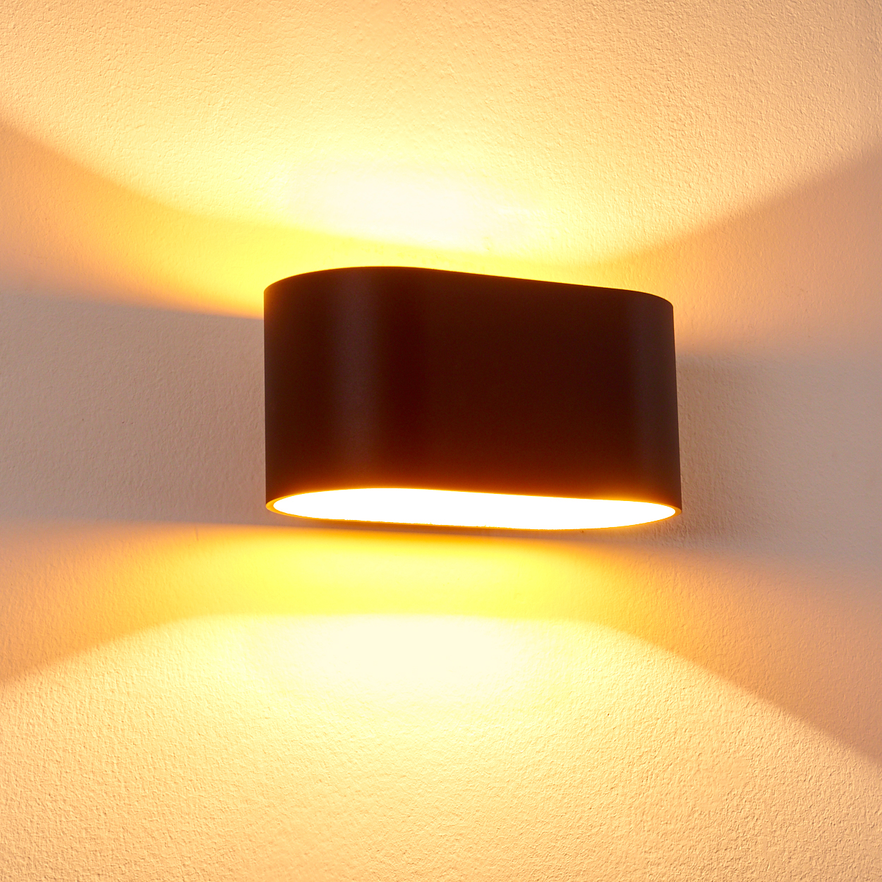 Dunkler Wandleuchter leuchtet nach oben und unten an einer cremefarbenen Wand.