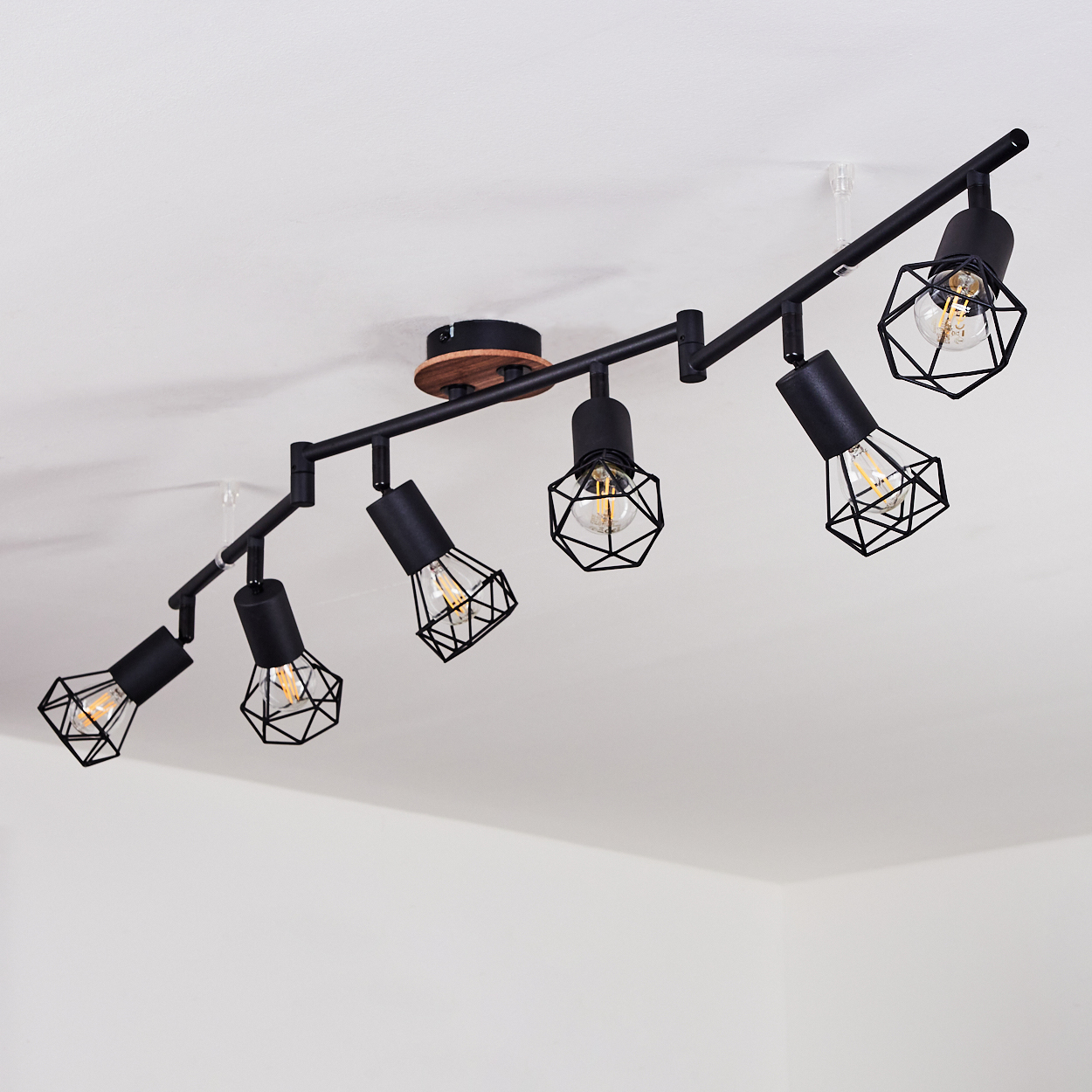 Eine schwarze Schienenleuchte mit sechs Lampen im Industrie-Stil mit Käfig an weißer Decke.