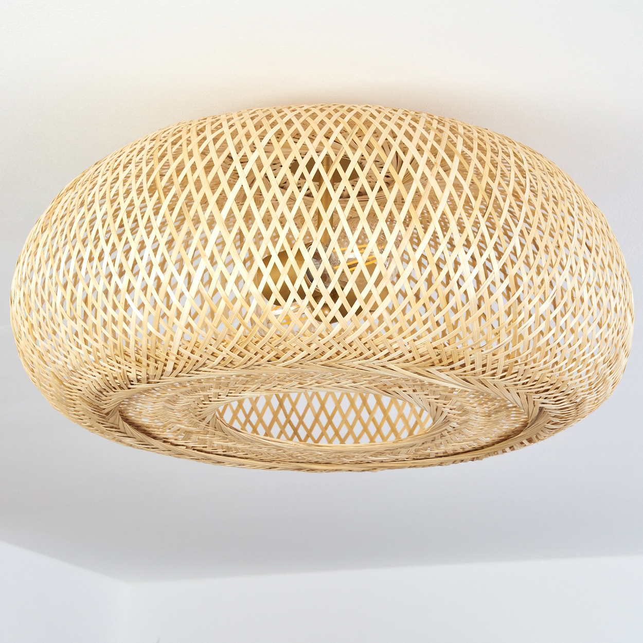 Eine runde, geflochtene Bambuslampe hängt an einer weißen Decke.