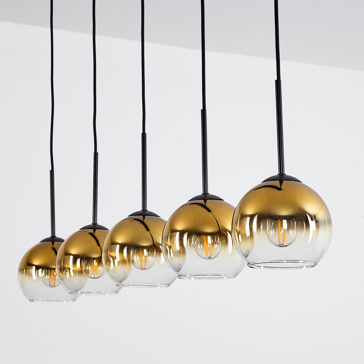 Fünf goldene Pendelleuchten mit durchsichtigen Glaskugeln und sichtbaren Glühbirnen.