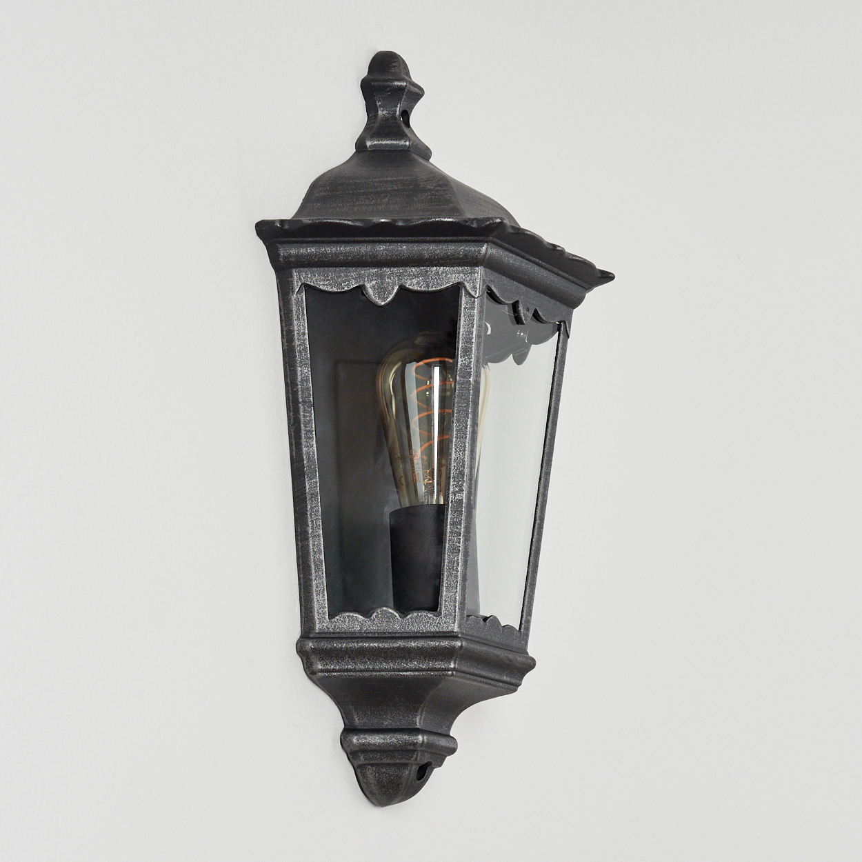 Eine dunkle Wandlaterne mit einem Edison-Glühbirne an einer weißen Wand.