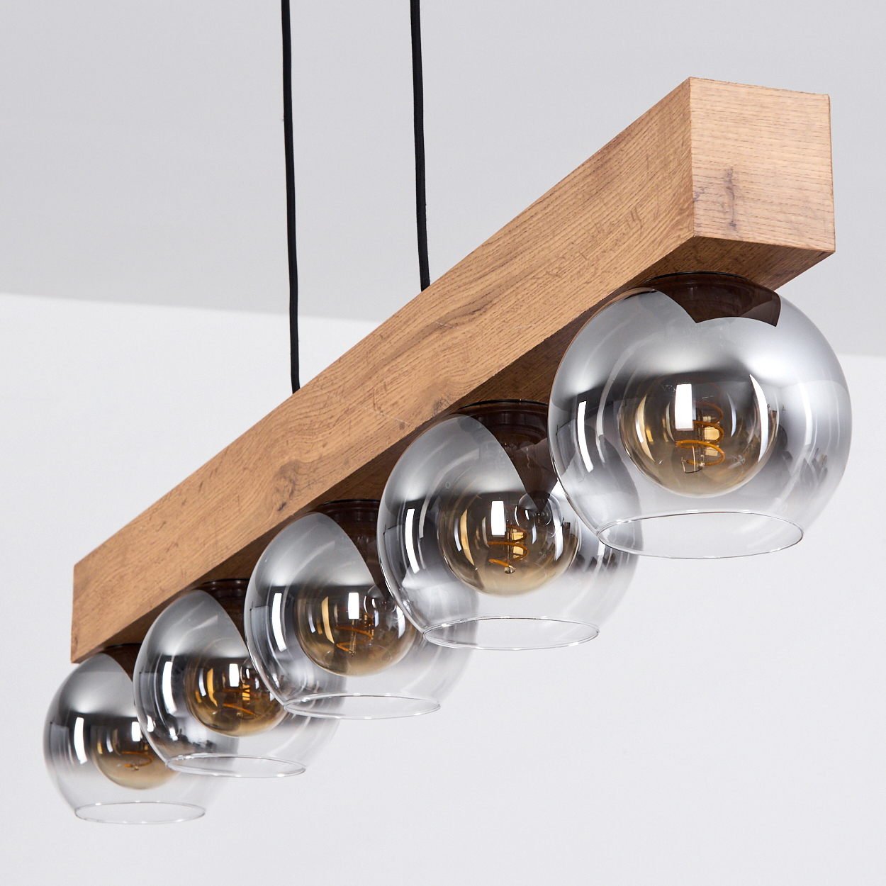 Holzbalken-Pendelleuchte mit fünf kugelförmigen Glaslampenschirmen und sichtbaren Glühbirnen.