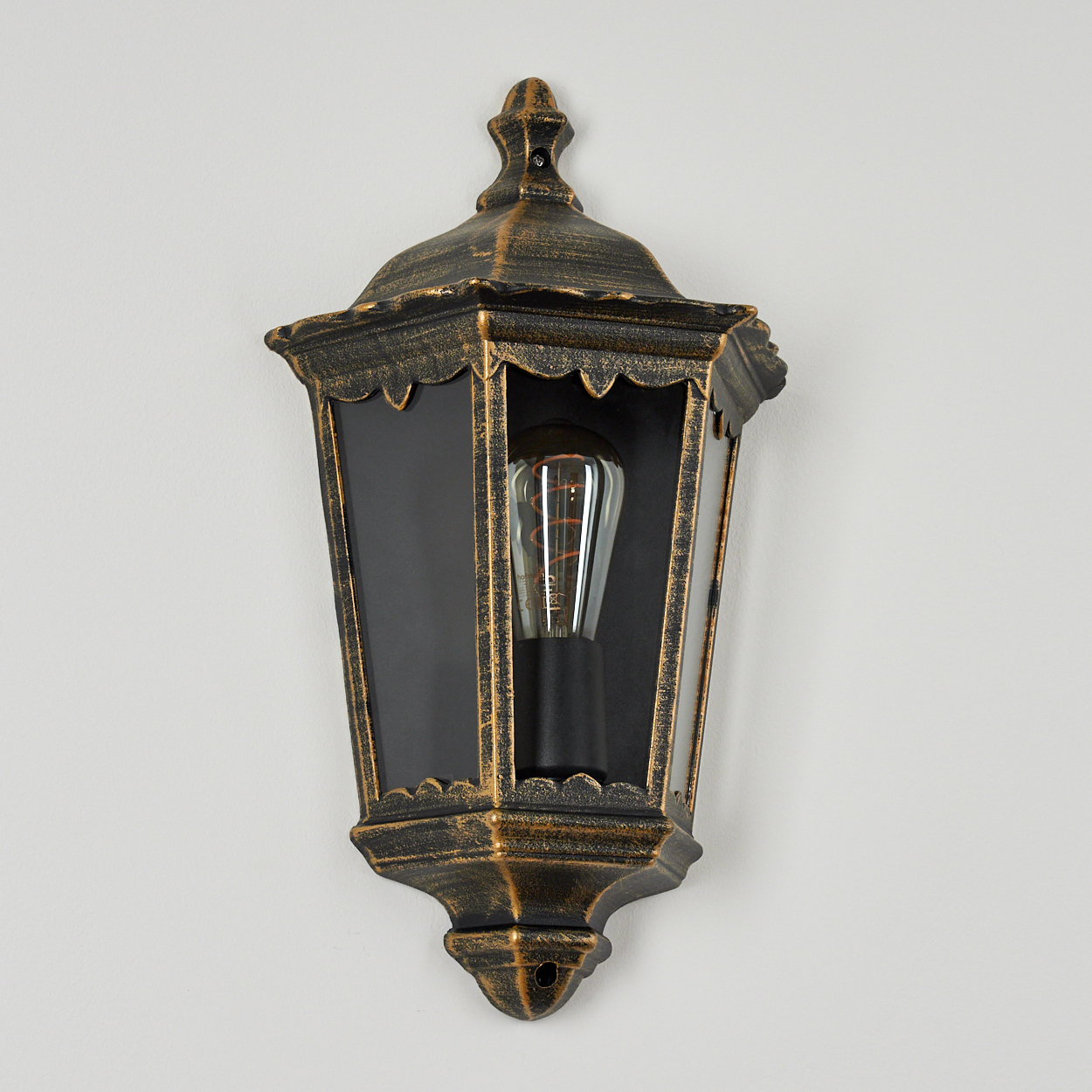 Eine bronzefarbene Wandlampe mit schwarzem Einsatz und sichtbarer Glühbirne.