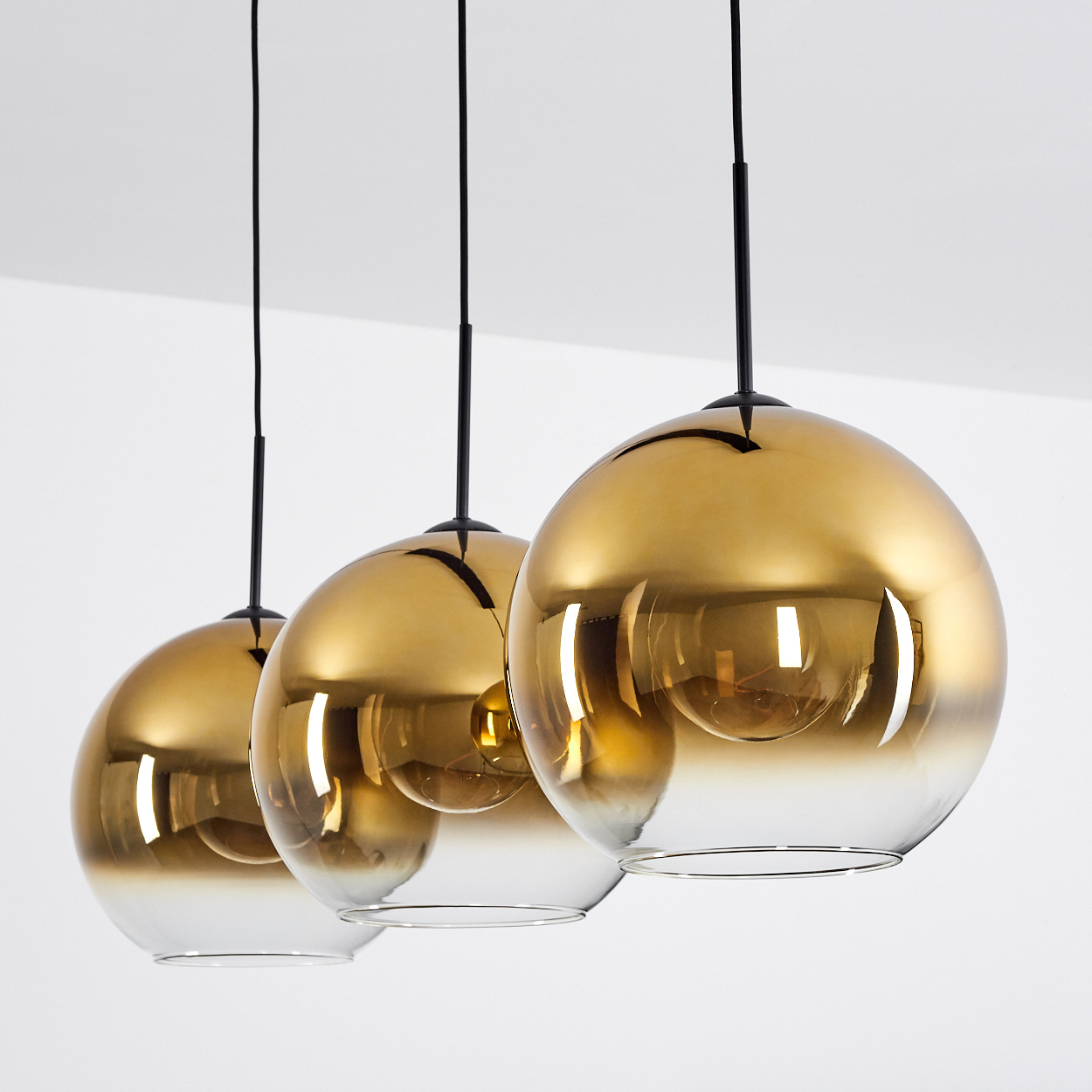 Drei goldene, glänzende Glaskugelleuchten mit weißen unteren Hälften.