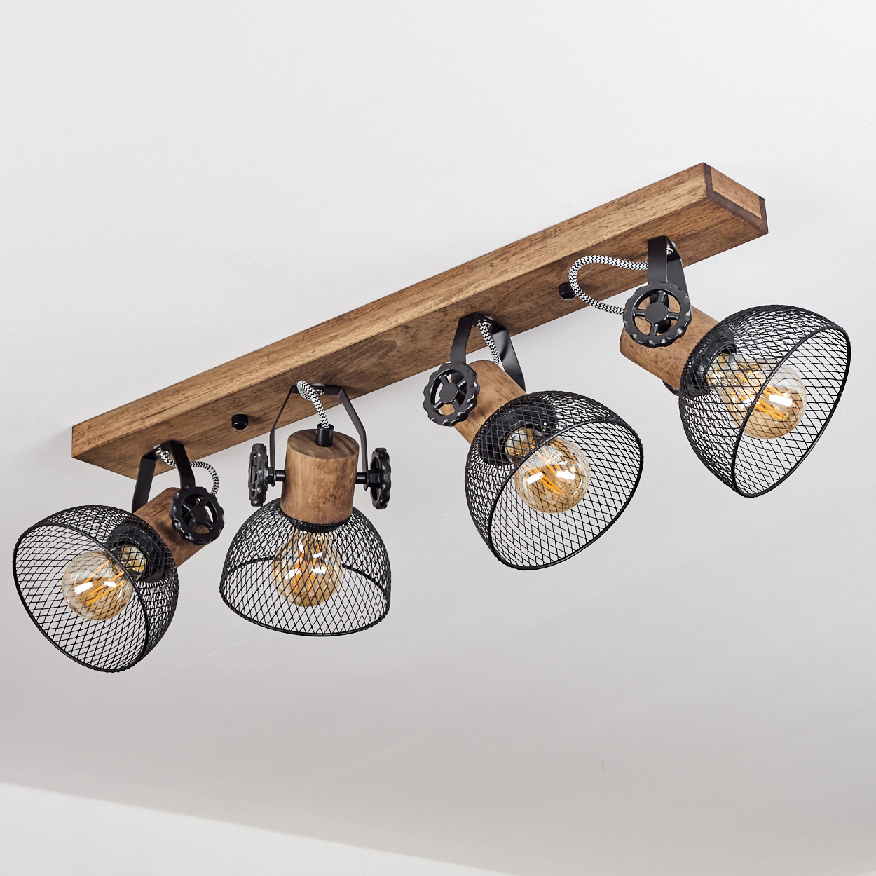 Ein Holzbalken mit vier schwarzen Strahlern im Industriestil, jeder mit einem Netzschirm.