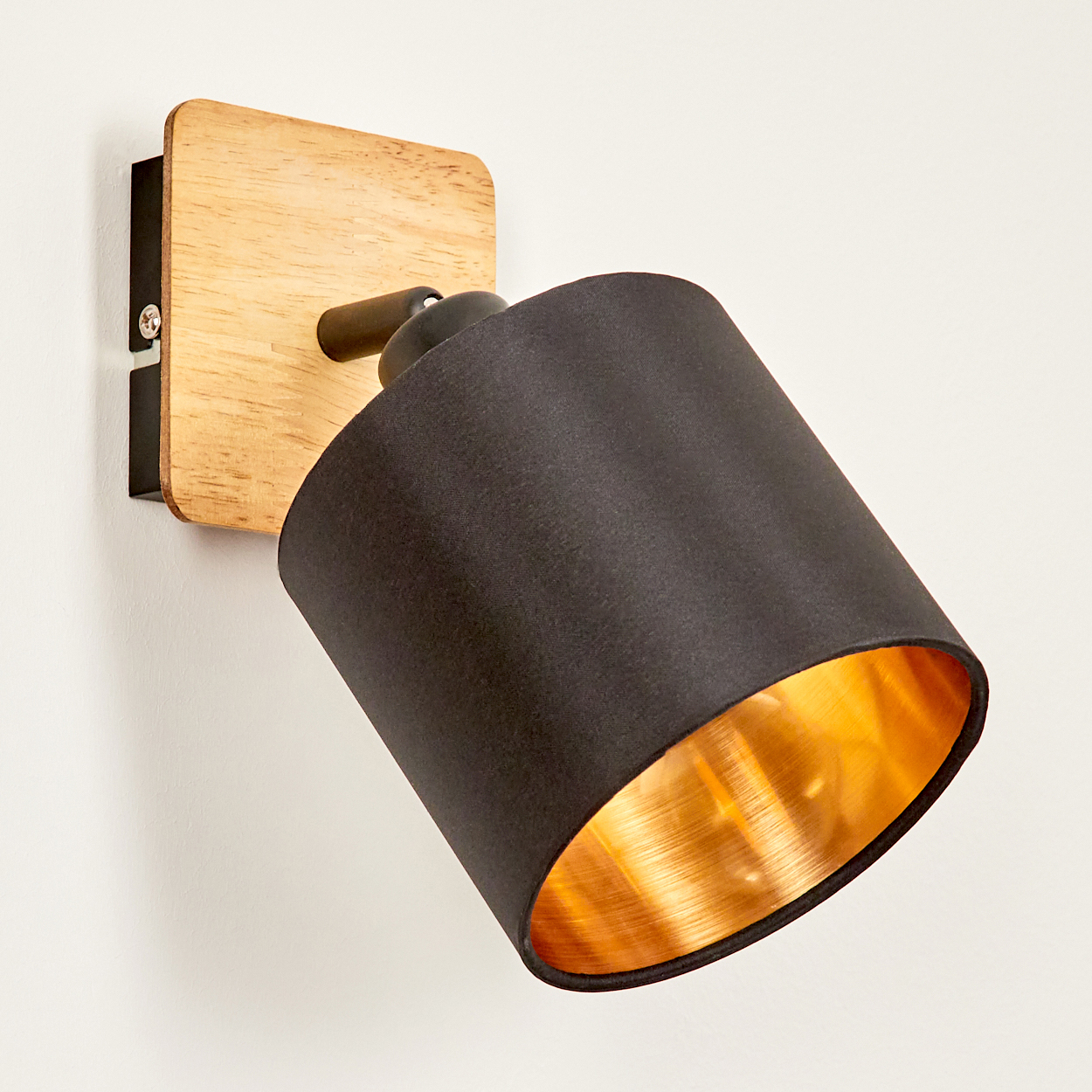 Eine Wandleuchte mit schwarzem Schirm und goldenem Inneren auf Holzsockel.