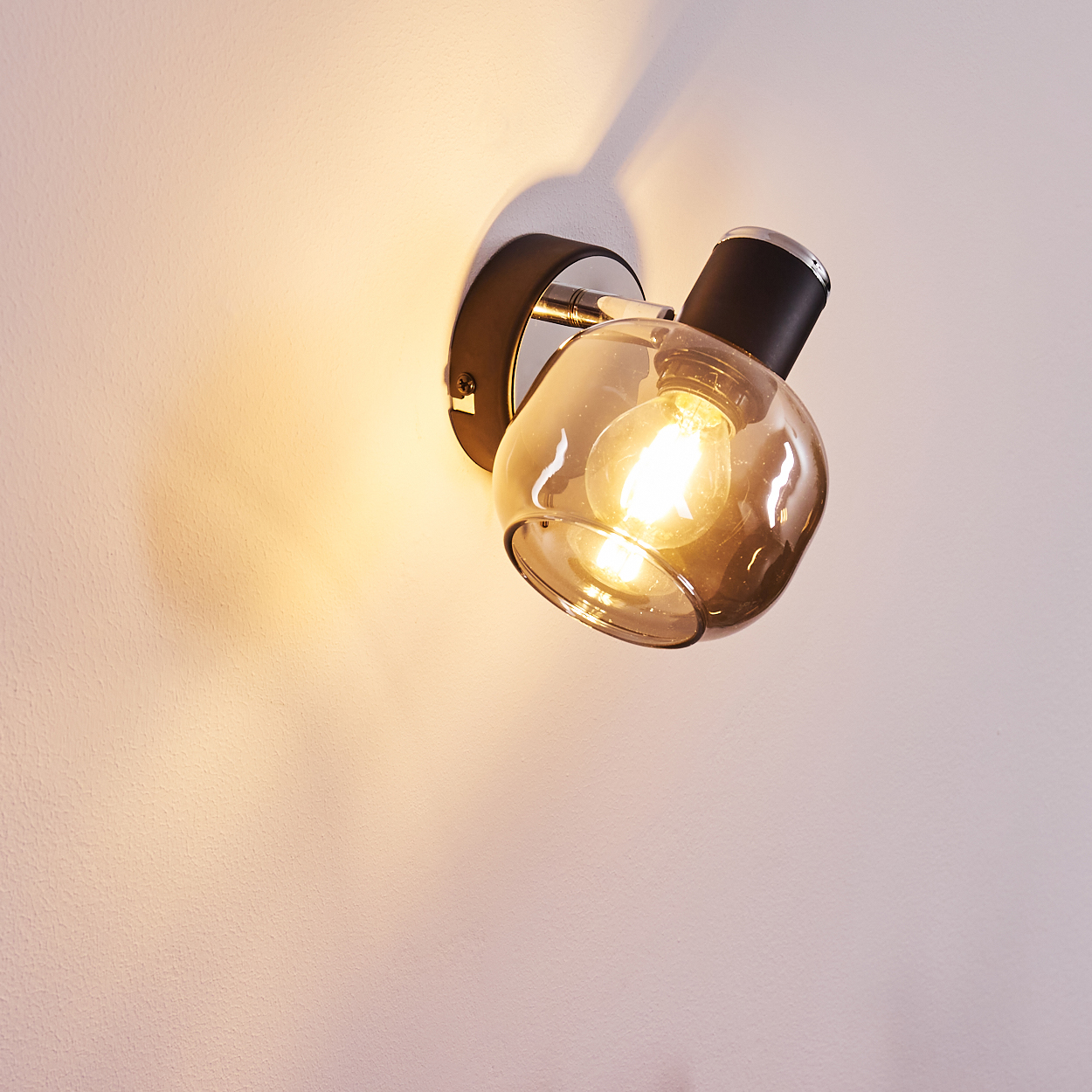 Eine Wandleuchte mit rauchigem Glas und sichtbarer Glühbirne leuchtet auf einer Wand.