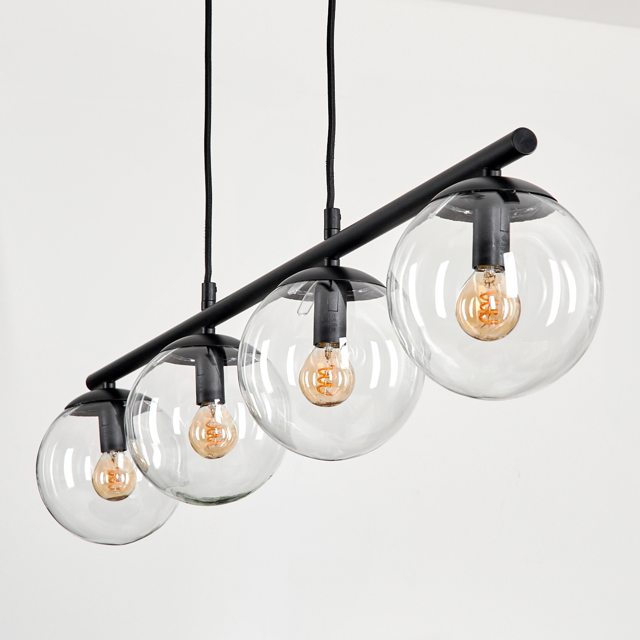Ein schwarzer linearer Kronleuchter mit vier Klarsichtglaskugeln, die jeweils eine Glühfadenlampe halten.
