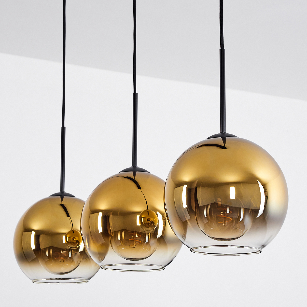 Drei goldene Pendelleuchten mit Glaskugeln und sichtbaren Glühbirnen.