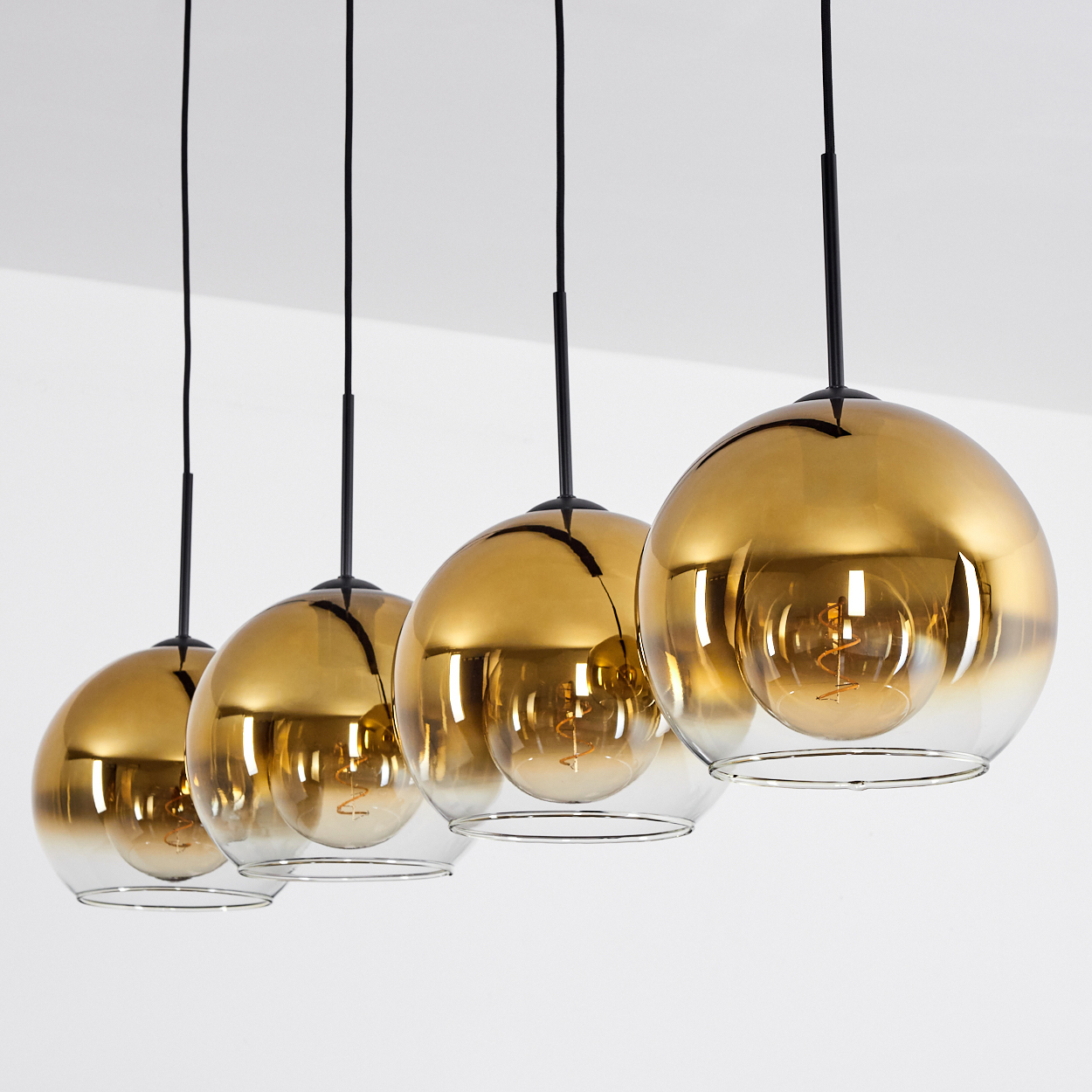 Fünf goldene Glaslampen mit sichtbaren Glühbirnen hängen an schwarzen Kabeln.