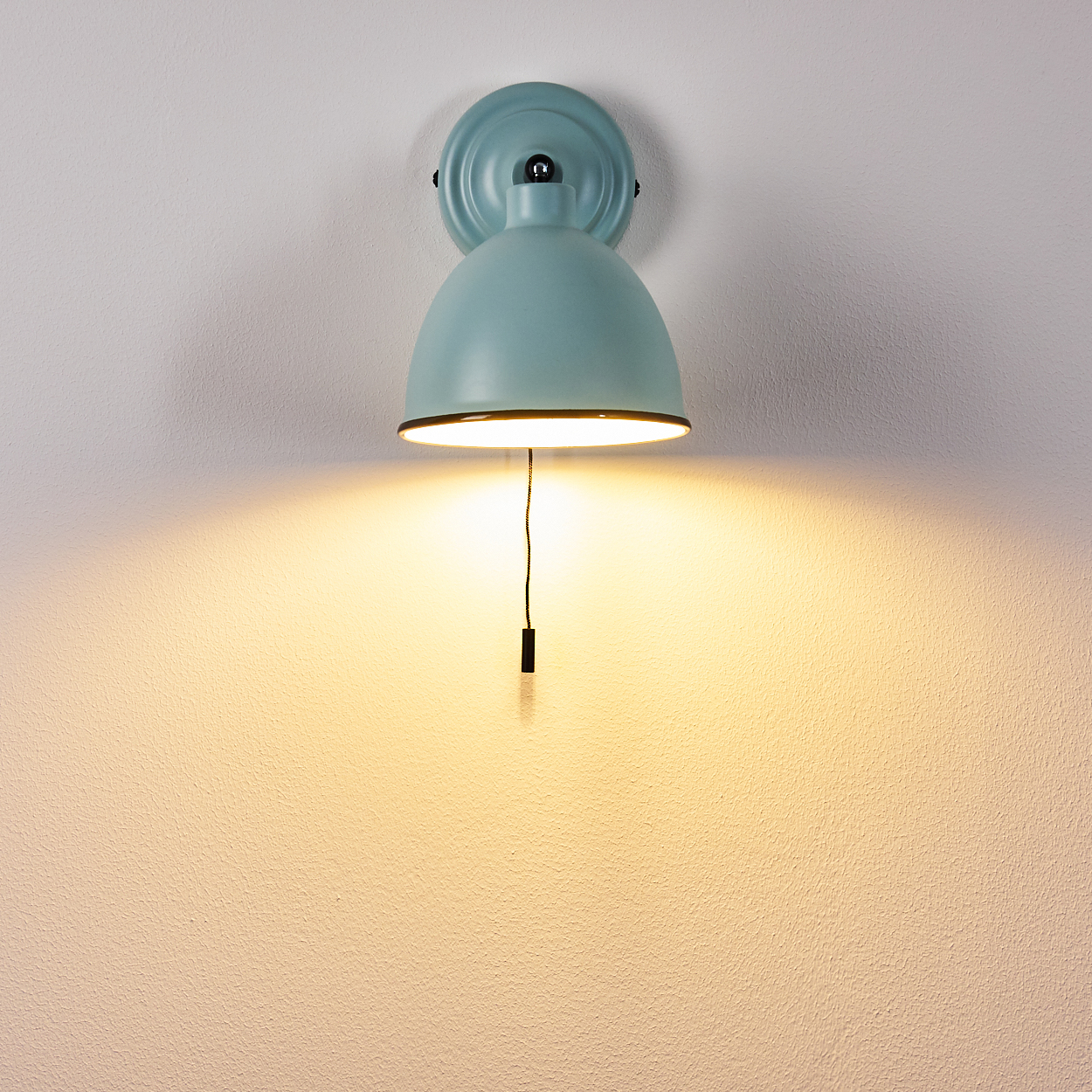 Ein blauer Wandlampenschirm leuchtet und wirft ein warmes Licht auf die Wand.