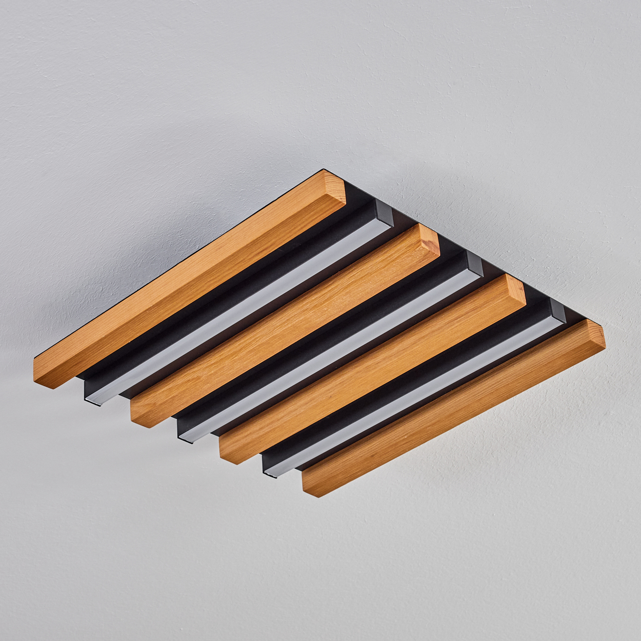 Deckenleuchte mit Holzlamellen und schwarzen Akzenten auf weißem Hintergrund.