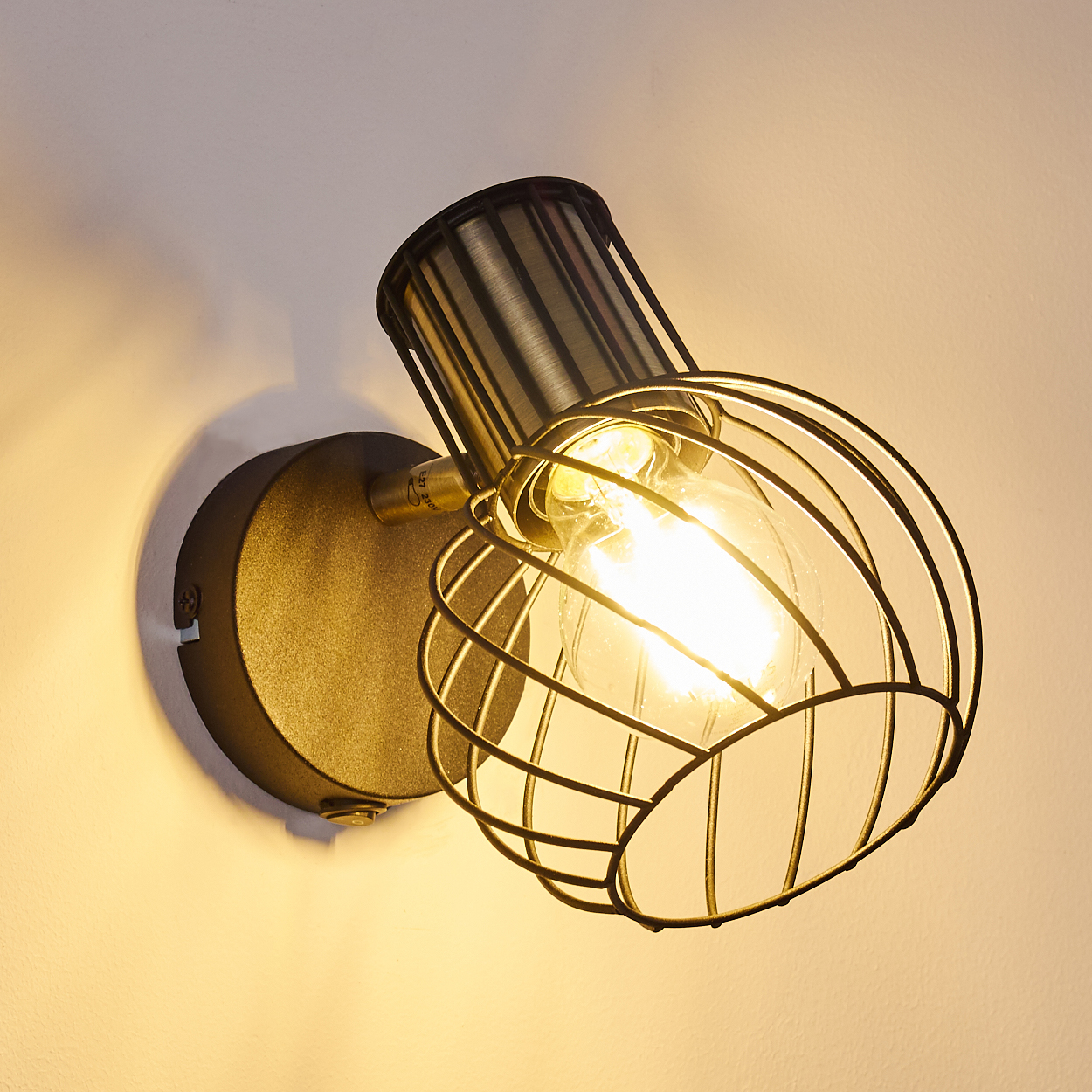 Eine Wandleuchte mit Metallkäfig und sichtbarer Glühbirne.