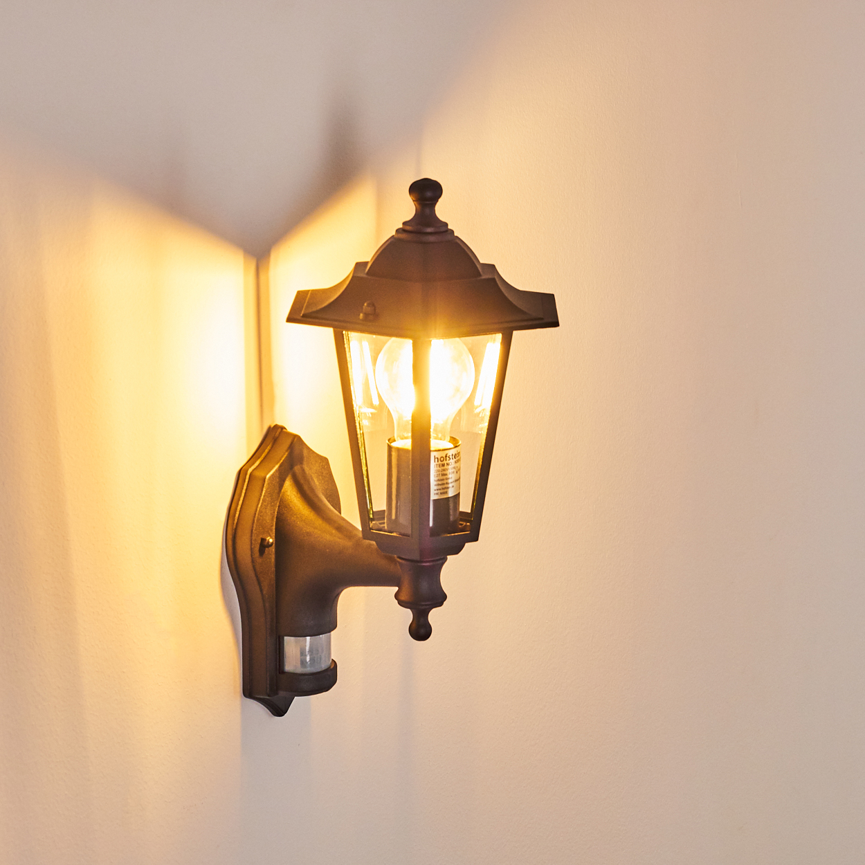 Eine dunkle Wandleuchte mit Bewegungsmelder und Glühbirne leuchtet an einer Wand.