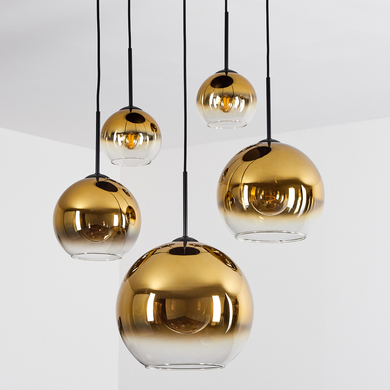 Fünf goldene Hängeleuchten mit Glaskugeln und sichtbaren Glühbirnen.