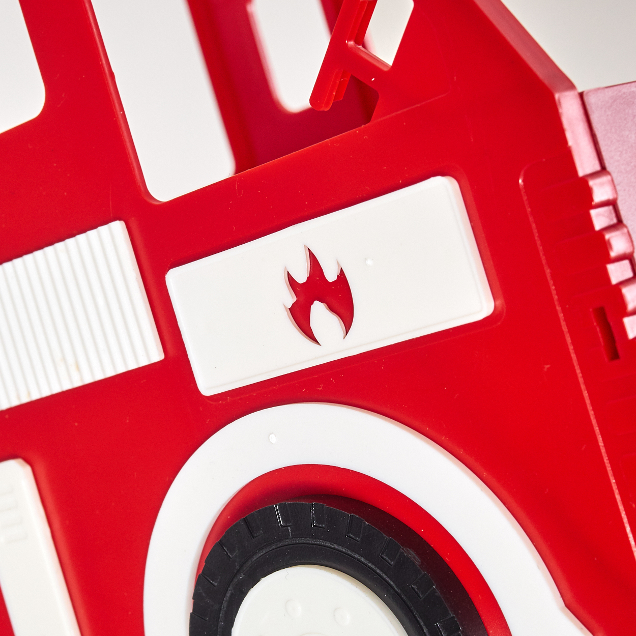 Rotes Spielzeug-Feuerwehrauto Seitenansicht mit Flammenemblem und Reifen.