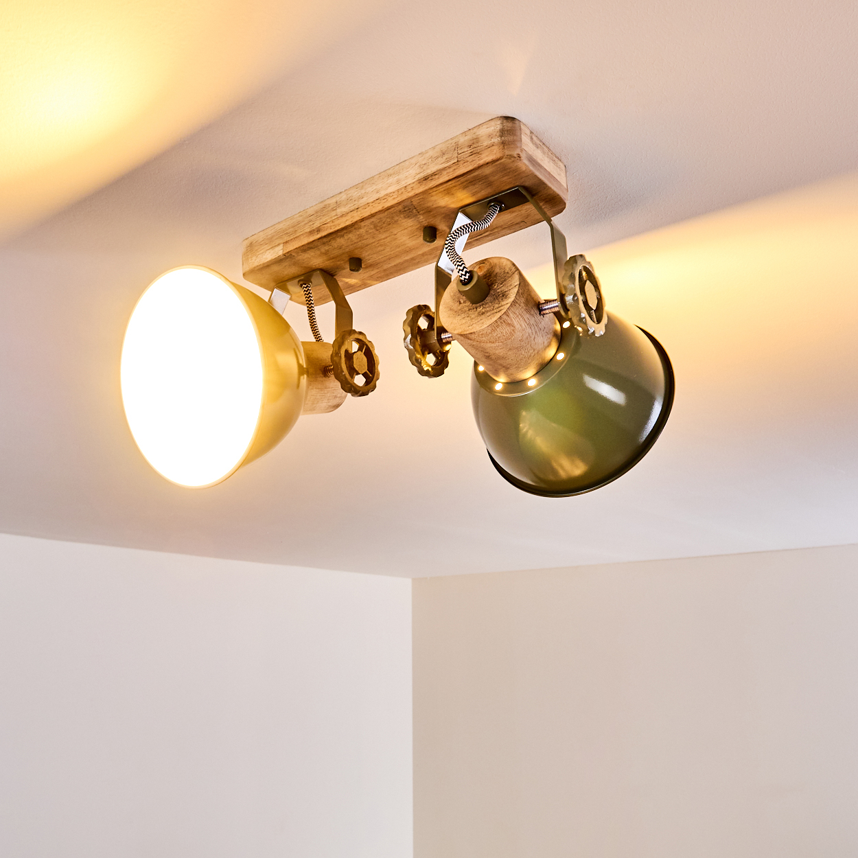 Eine rustikale Deckenleuchte mit zwei verstellbaren Lampen, eine goldene, eine grüne, auf Holzsockel.