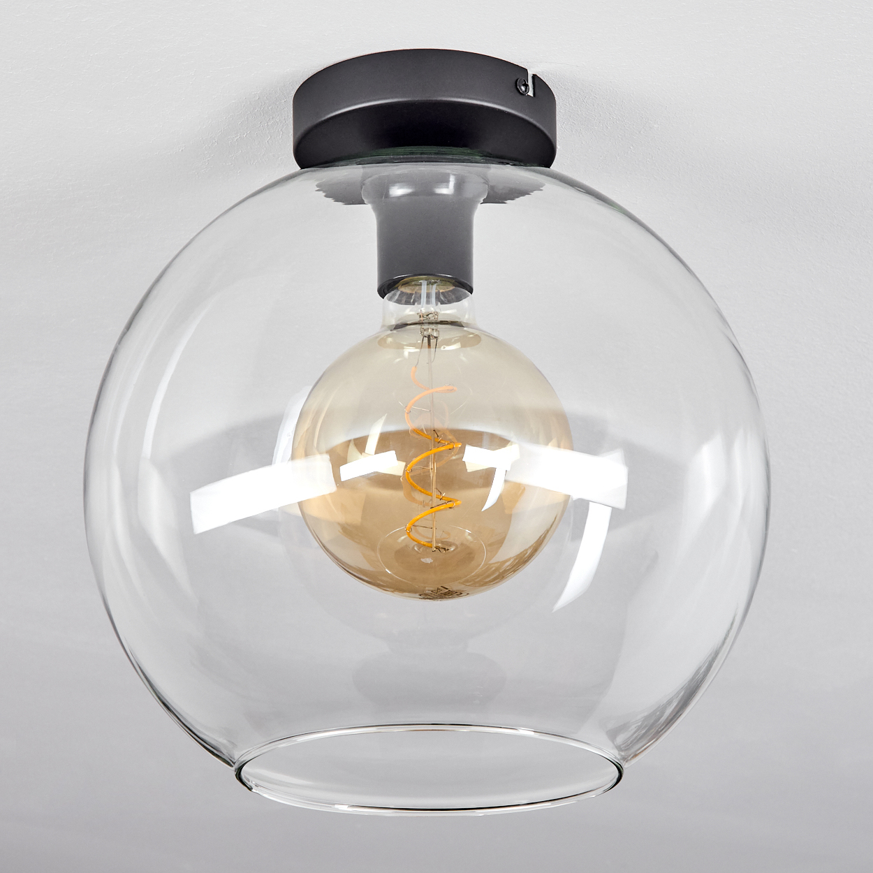 Eine klare Glaskugel-Lampe mit einer Edison-Glühbirne und einem dunklen Sockel.