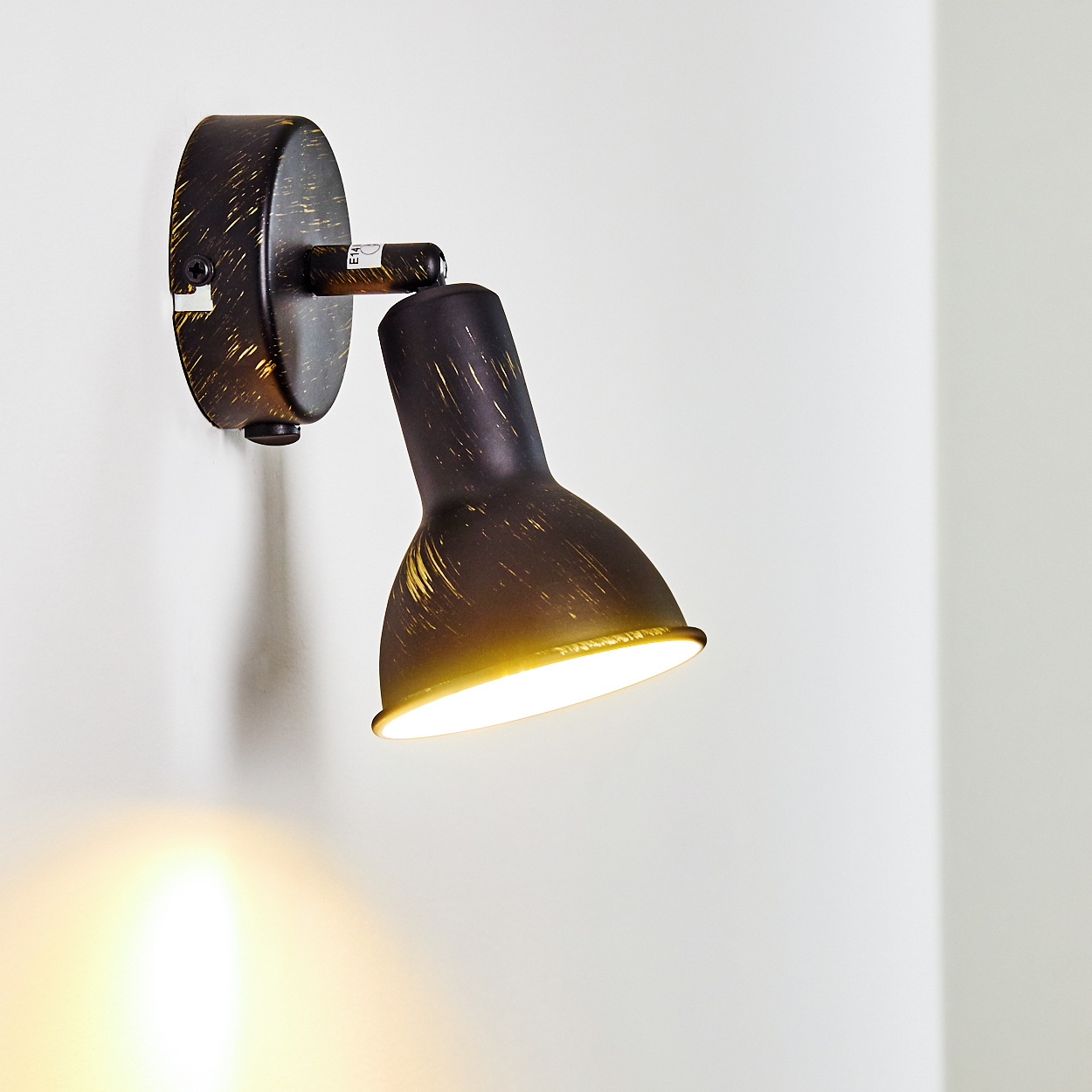 Eine dunkle Wandleuchte mit goldfarbenen Sprenkeln leuchtet.