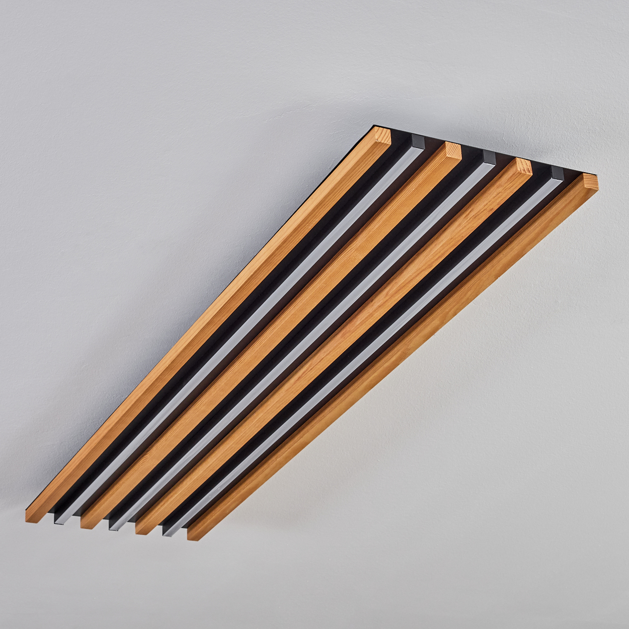 Ein Holzlattenpaneel mit schwarzen und grauen Streifen an einer hellgrauen Wand.