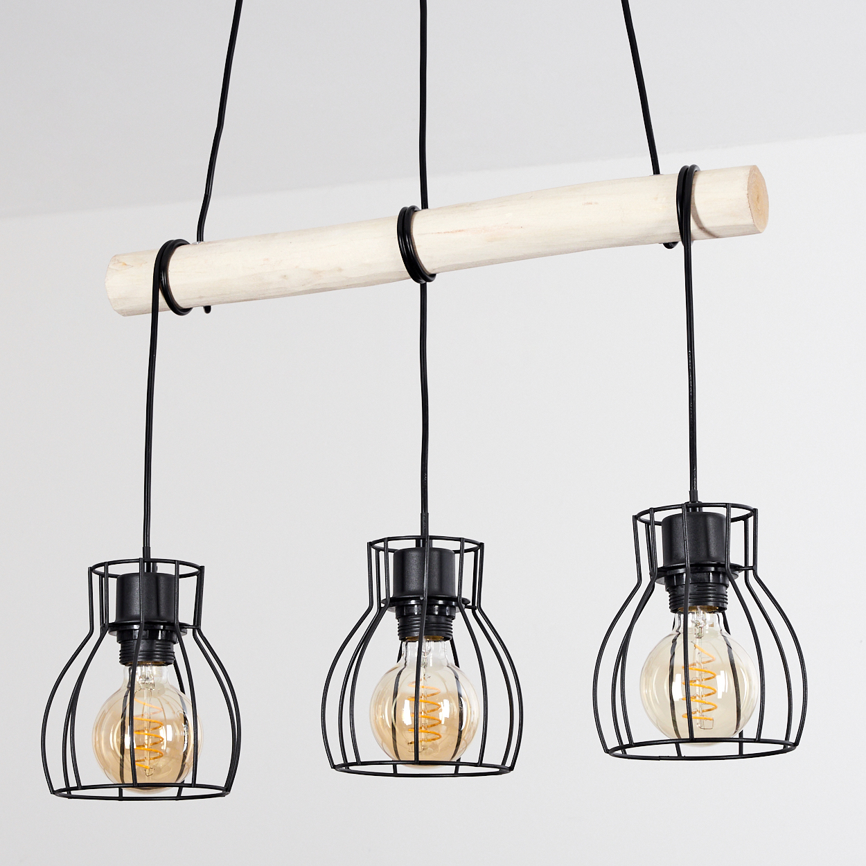 Drei Pendelleuchten mit schwarzen Drahtkäfigen und Edison-Glühbirnen hängen von einem Holzbalken.