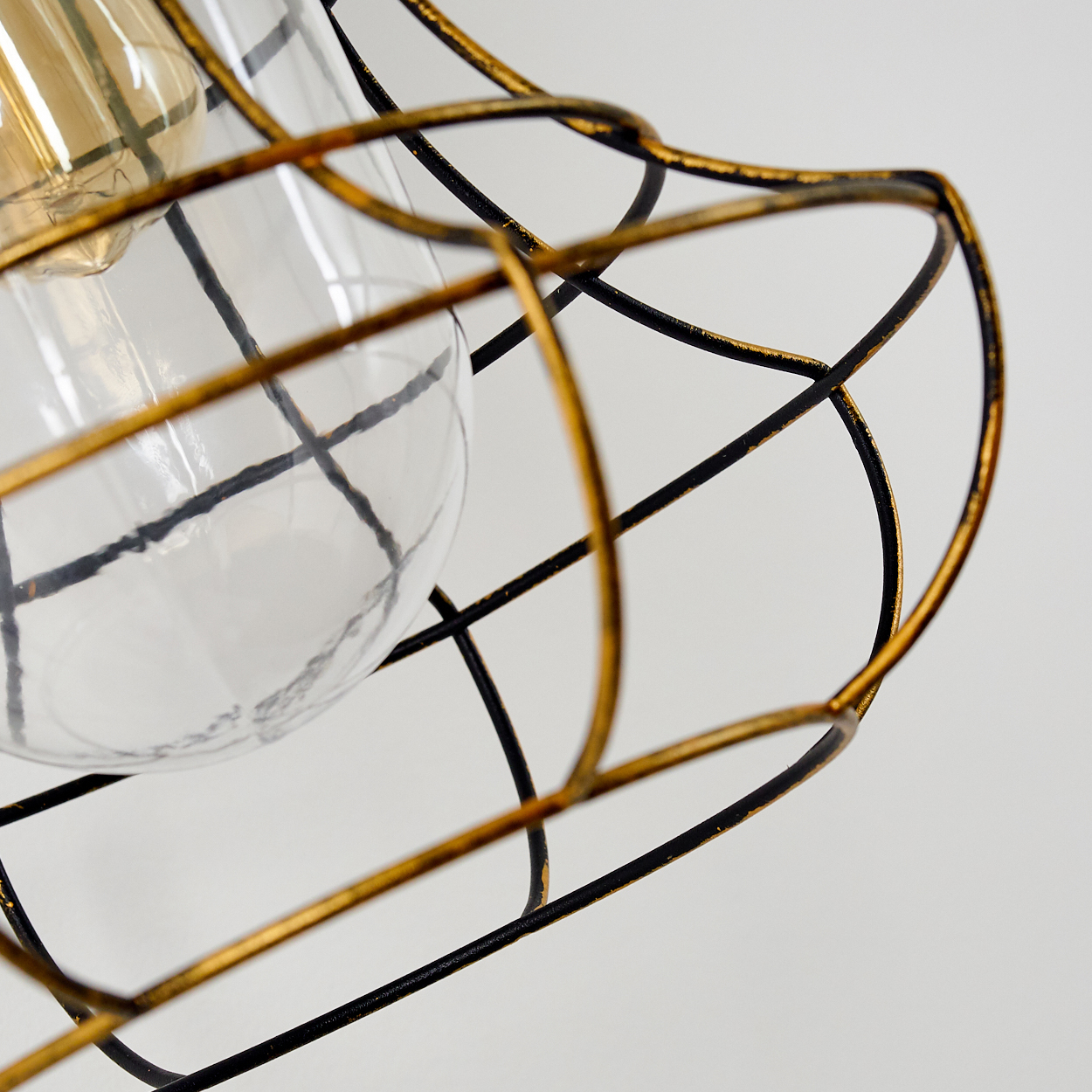 Nahaufnahme einer Glühbirne mit Drahtkäfigschutz in Gold und Schwarz.