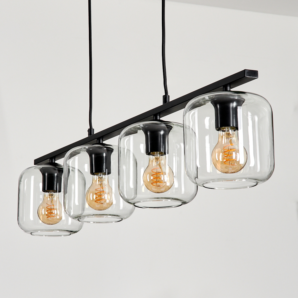 Ein moderner schwarzer linearer Kronleuchter mit vier klaren Glasschirmen und Edison-Glühbirnen.