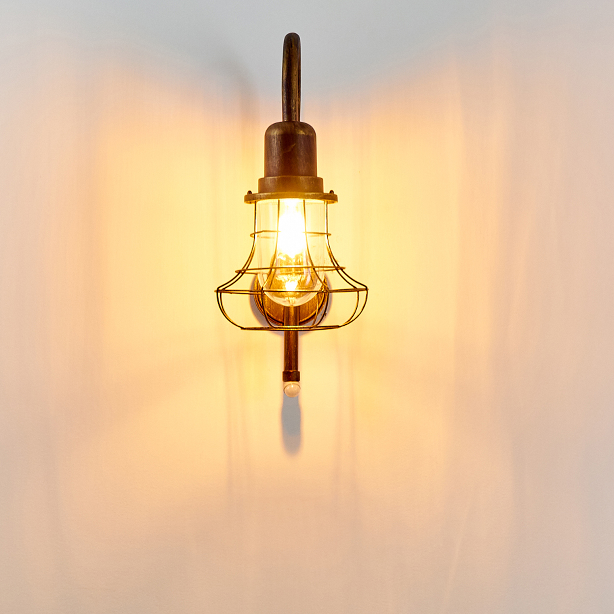 Eine Wandleuchte im Vintage-Stil mit Messing-Finish, Glasschirm und Drahtkorb.