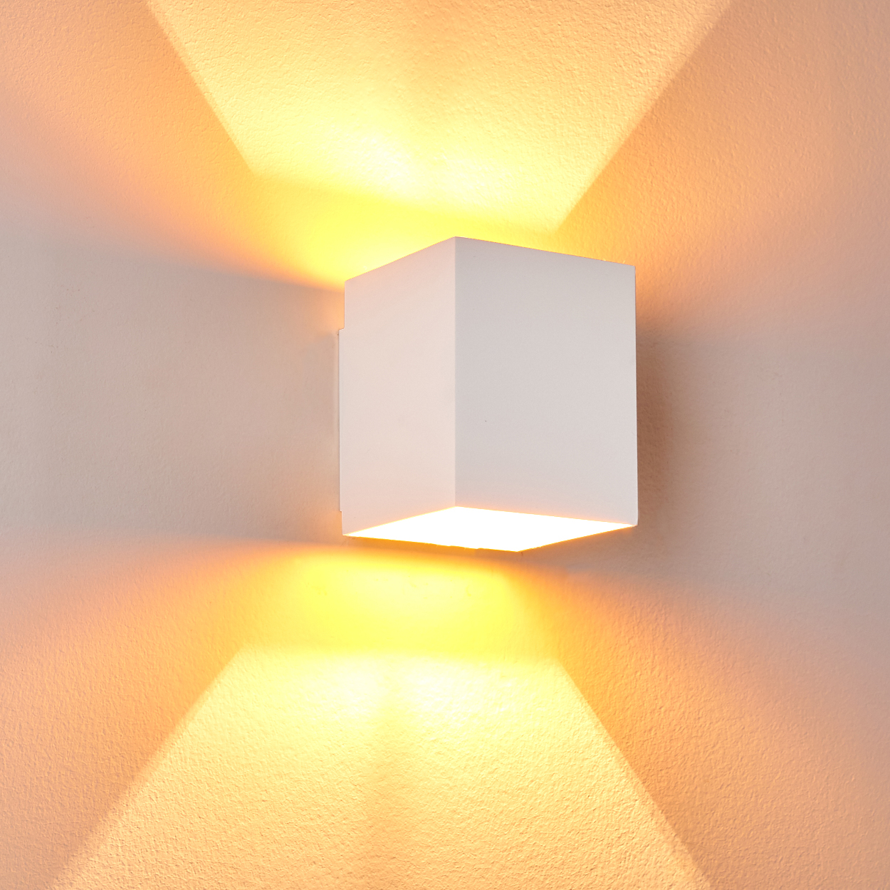 Ein weißer Würfel-Wandleuchter beleuchtet eine Wand mit warmem, gelbem Licht nach oben und unten.
