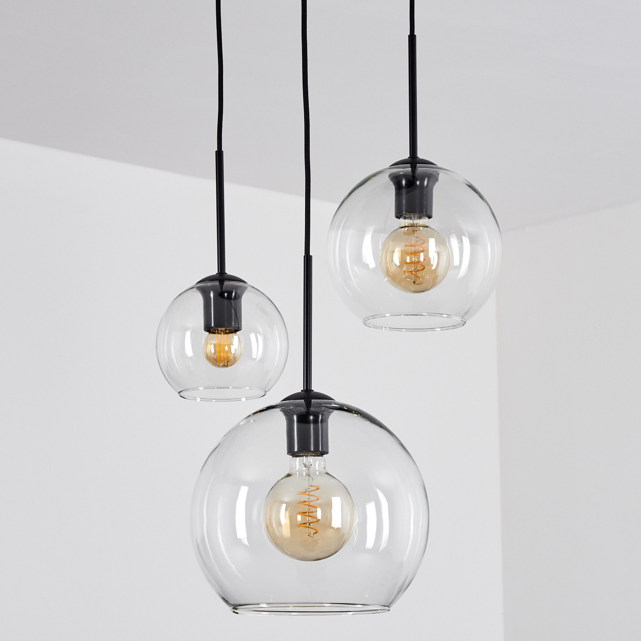 Drei Pendelleuchten aus klarem Glaskugel mit Edison-Glühbirnen hängen an schwarzen Kabeln.