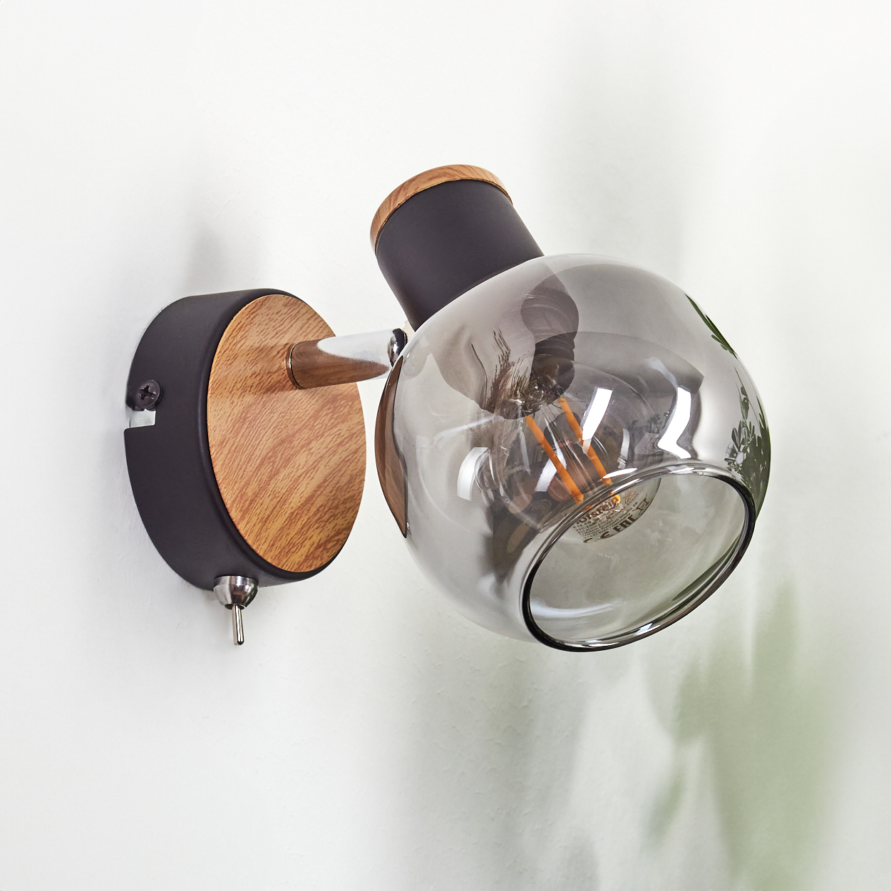 Eine Wandleuchte mit Holzsockel, schwarzem Arm und Rauchglas-Lampenschirm.