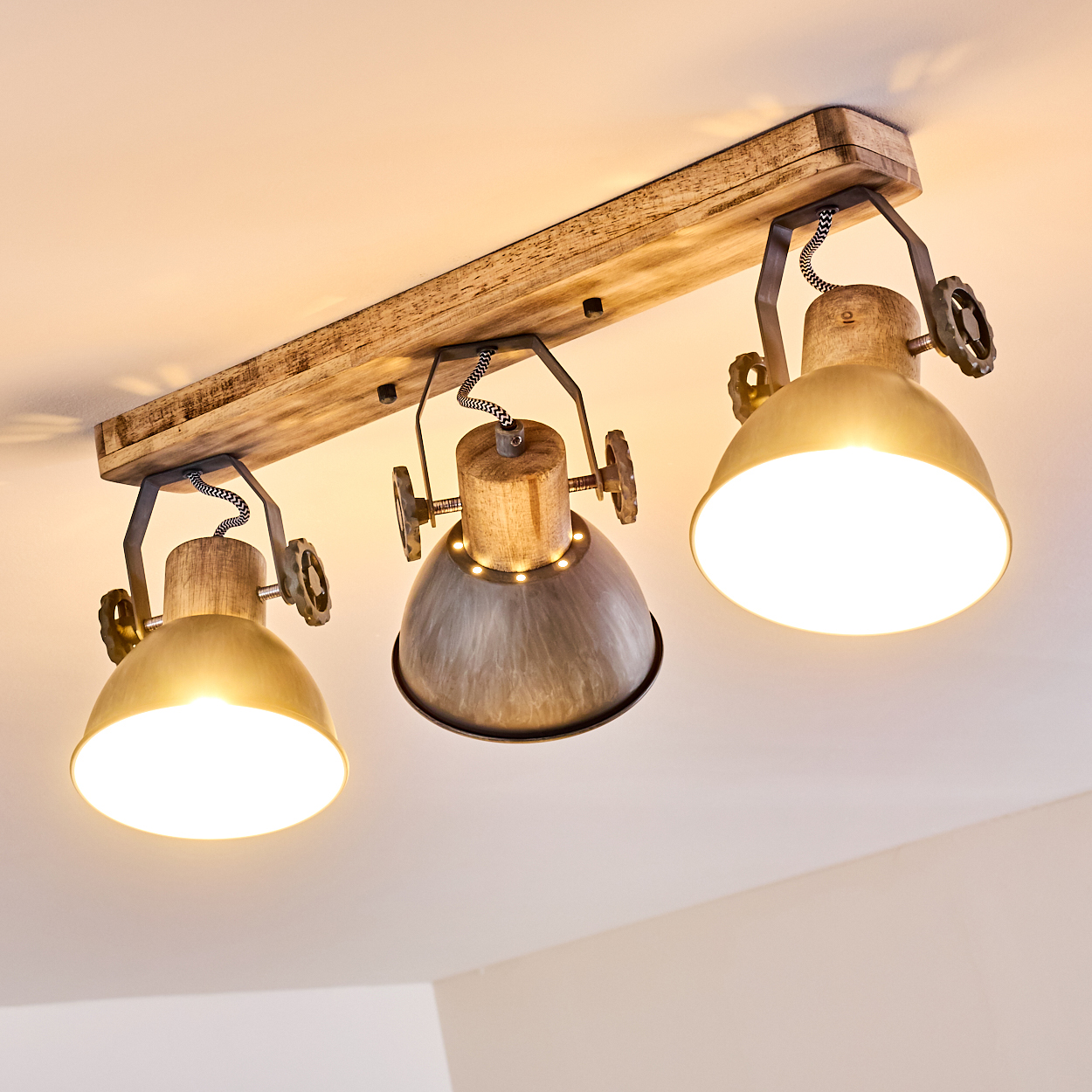 Deckenleuchte mit Holzbalken und drei Lampenschirmen in Gold und Grau.