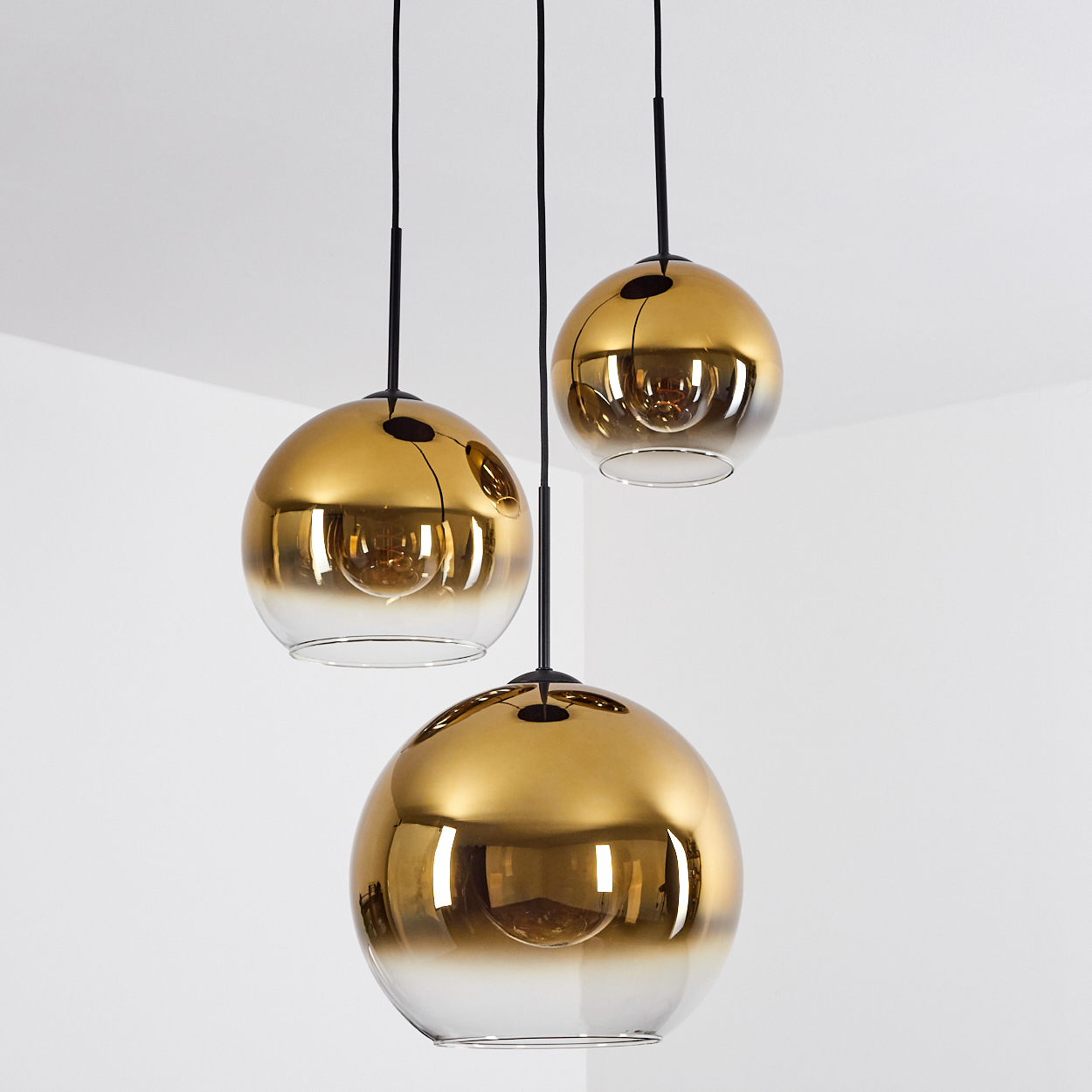 Drei kugelförmige Pendelleuchten aus gold-verlaufenem Glas hängen an schwarzen Kabeln.