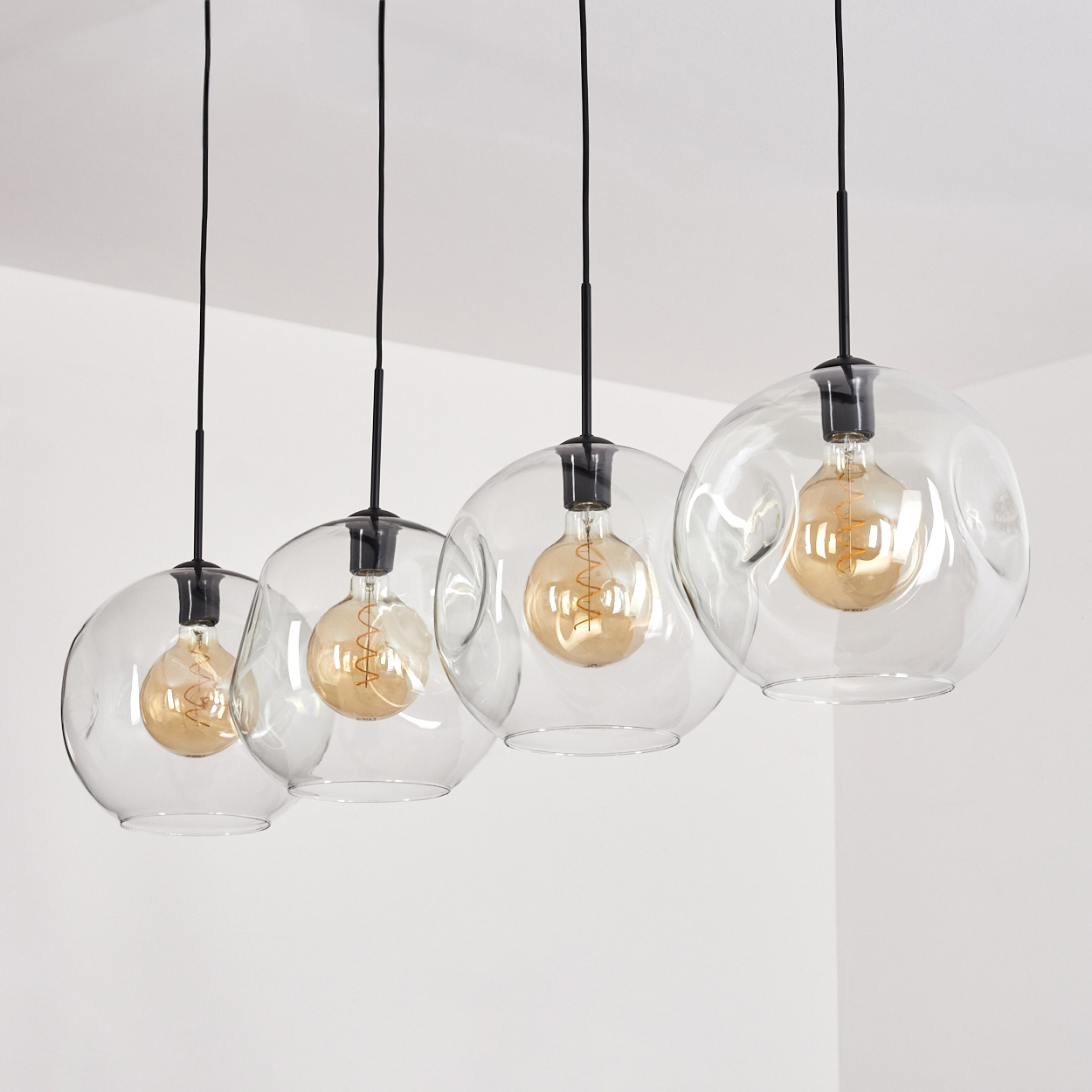 Vier klare Glaskugelleuchten mit Edison-Glühbirnen hängen von schwarzen Kabeln.