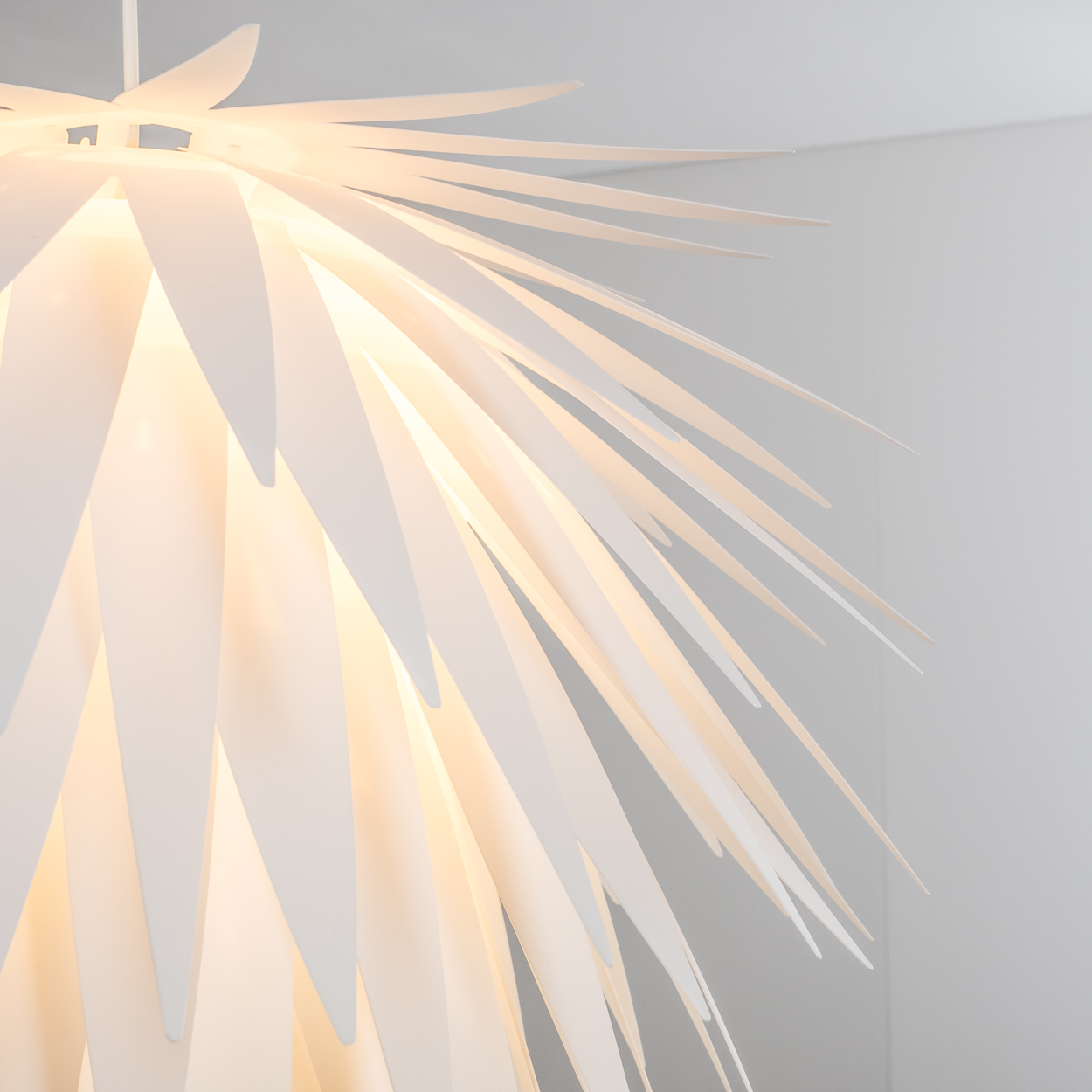 Eine weiße Lampe mit spitzen, sich überlappenden Lamellen, die wie eine Ananas aussehen.