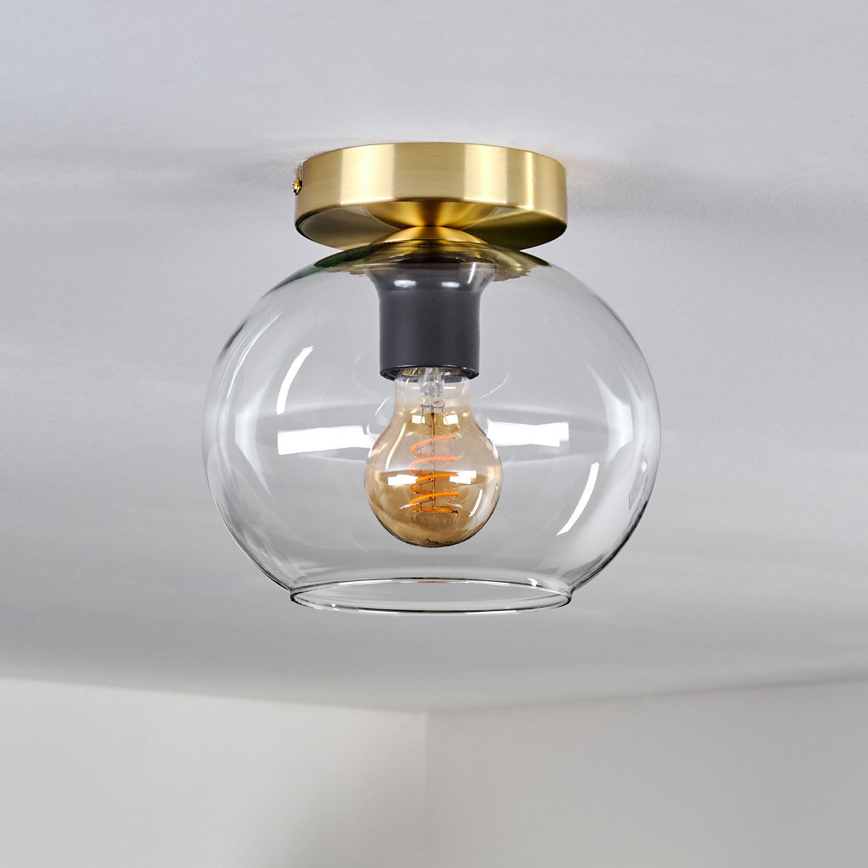 Eine Glühbirne mit goldenem Sockel und Glaskuppel an einer Decke.