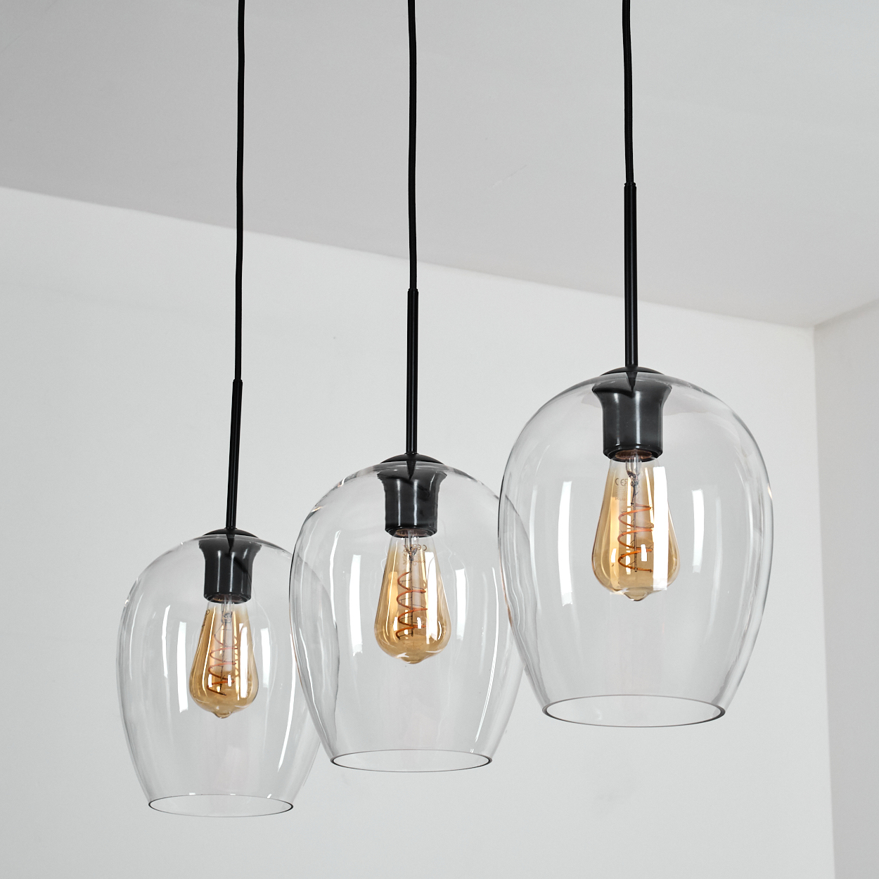 Drei Pendelleuchten mit klaren Glaskolben und Edison-Glühbirnen hängen von schwarzen Kabeln.