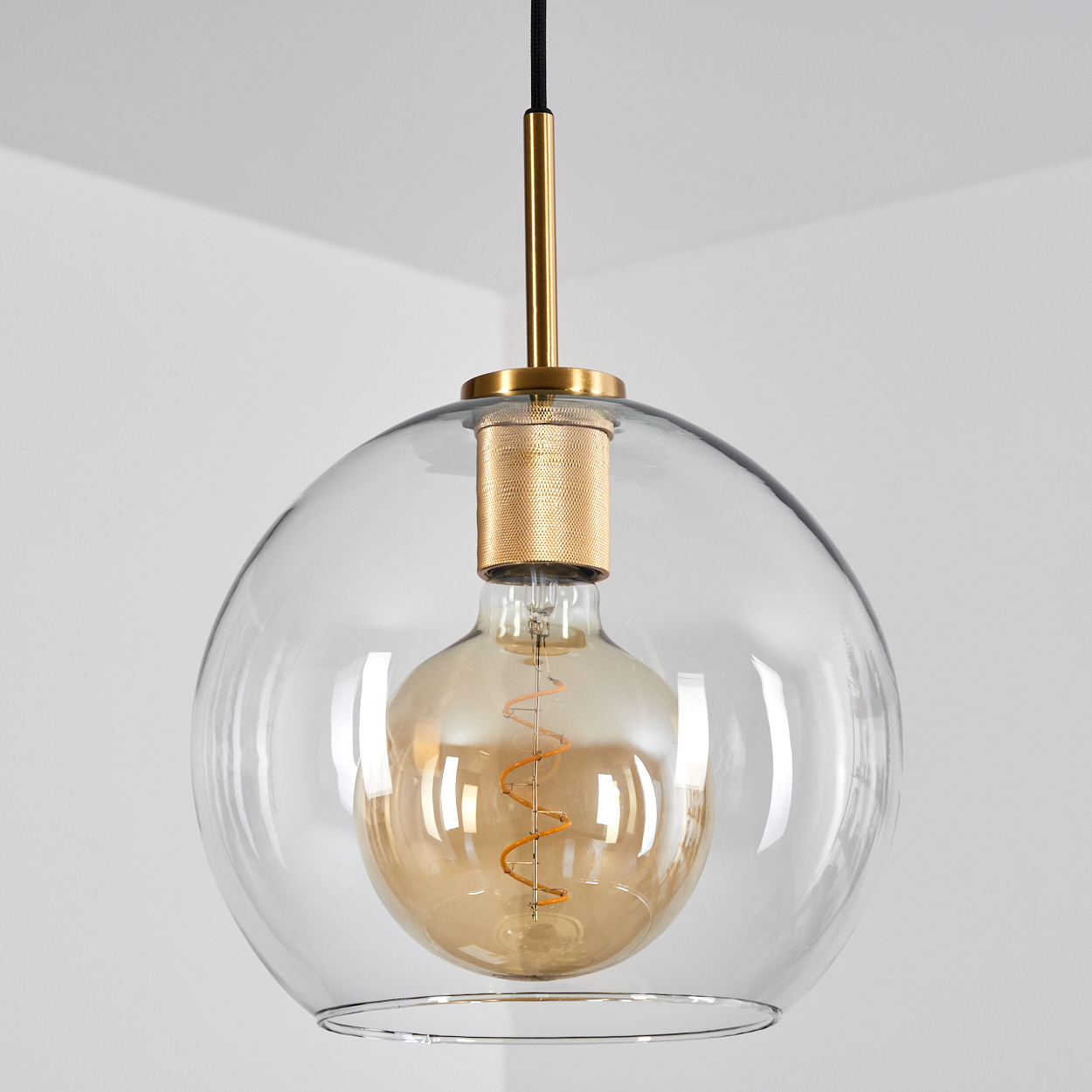 Eine goldene Glühbirne in einer transparenten Glaskugel-Pendelleuchte.