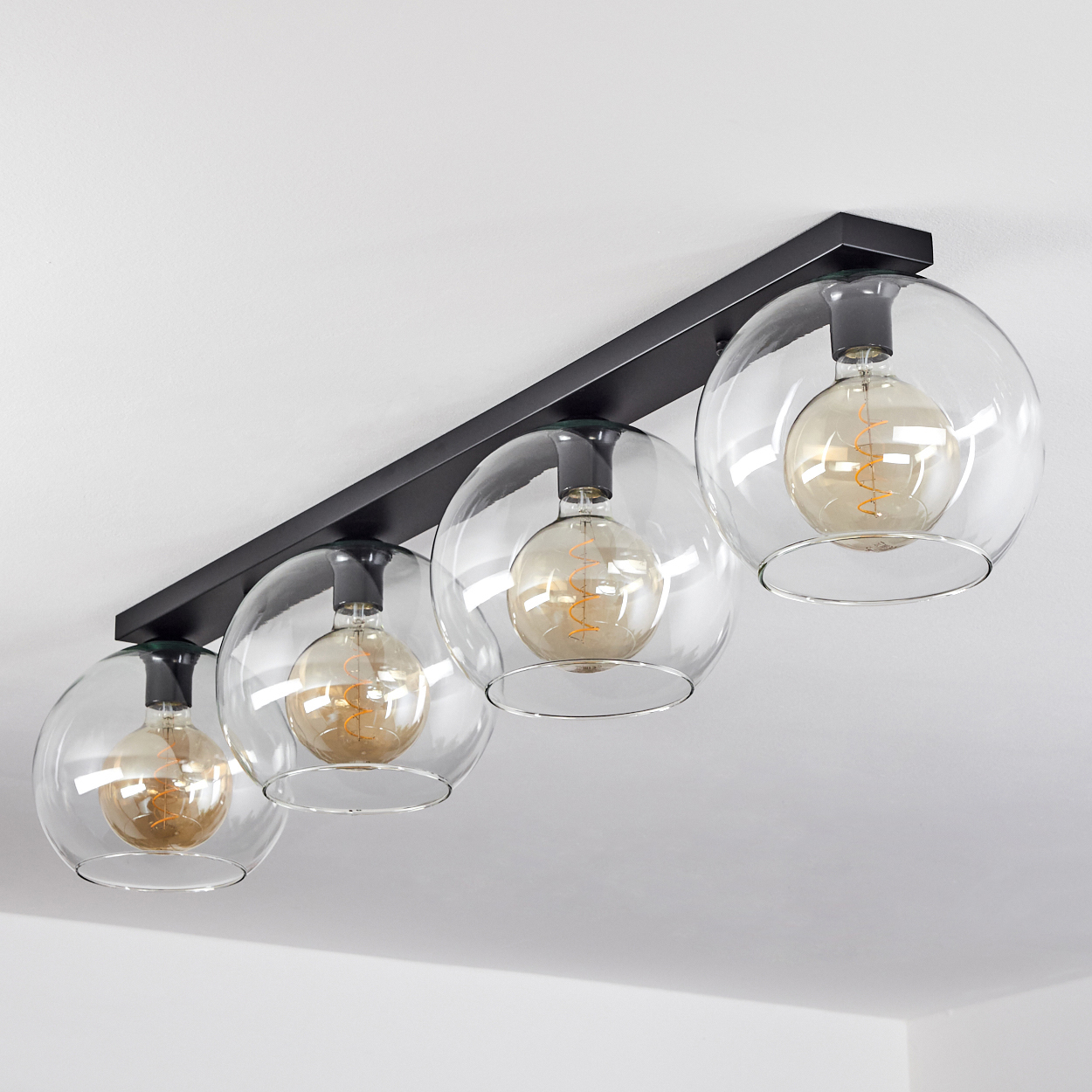 Eine moderne schwarze Leuchte mit vier klaren Glaskugeln und Edison-Glühbirnen.