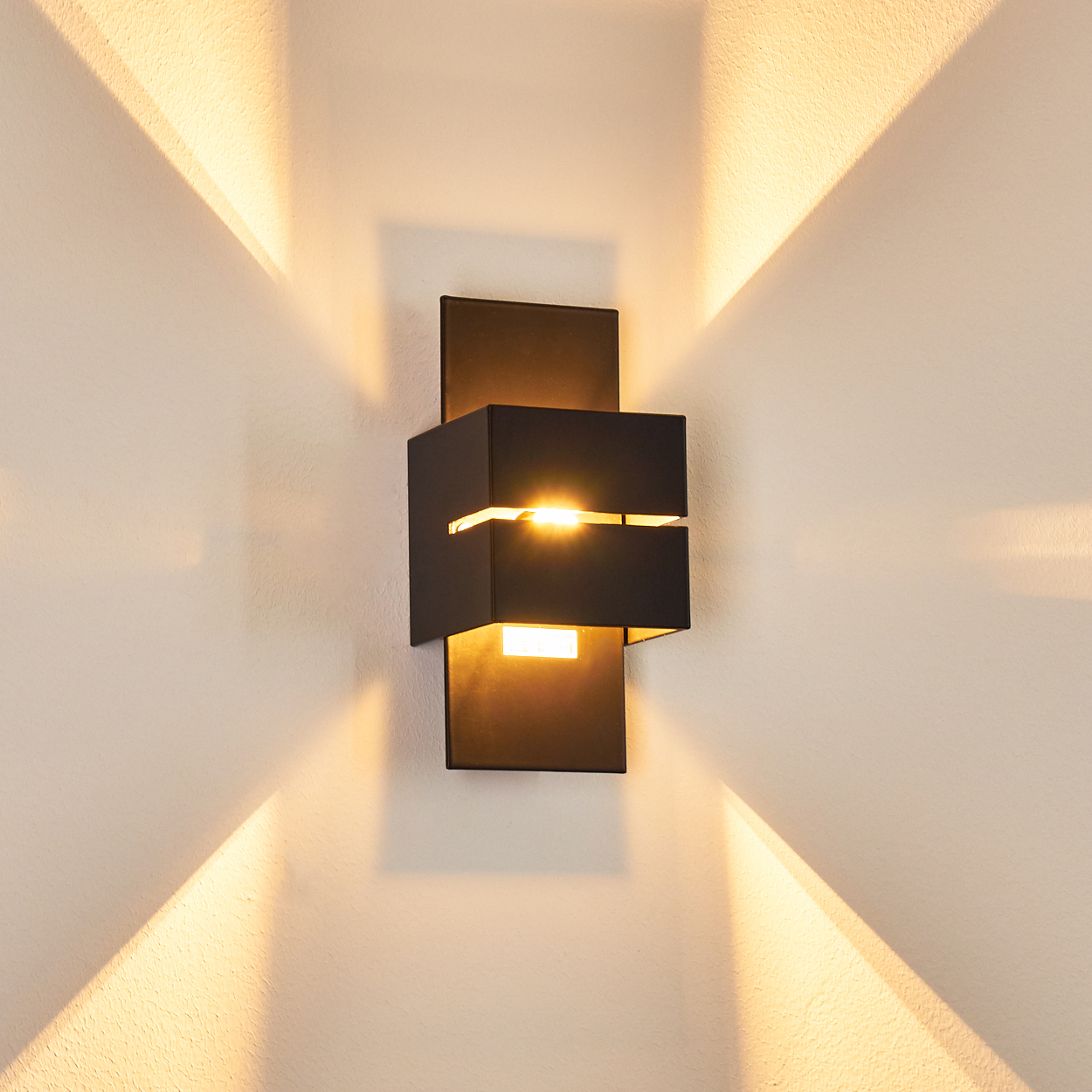 Ein moderner schwarzer Wandleuchter beleuchtet eine weiße Wand mit Lichtstrahlen.