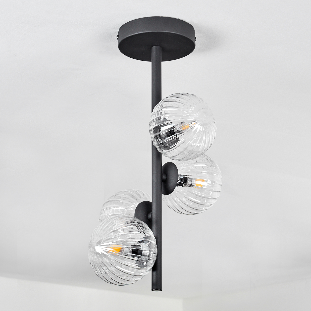 Eine moderne schwarze Deckenleuchte mit vier gerippten Glaskugeln, die jeweils eine LED-Birne halten.