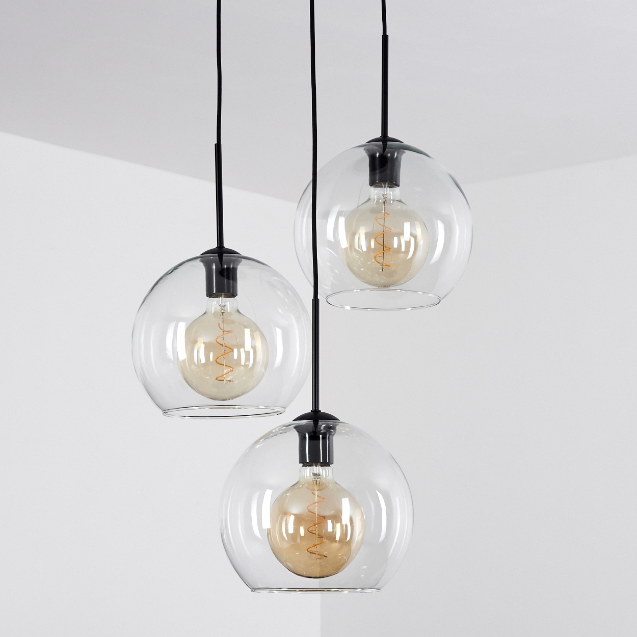 Drei Pendelleuchten mit Glaskugeln und sichtbaren Glühfadenlampen hängen von schwarzen Kabeln.