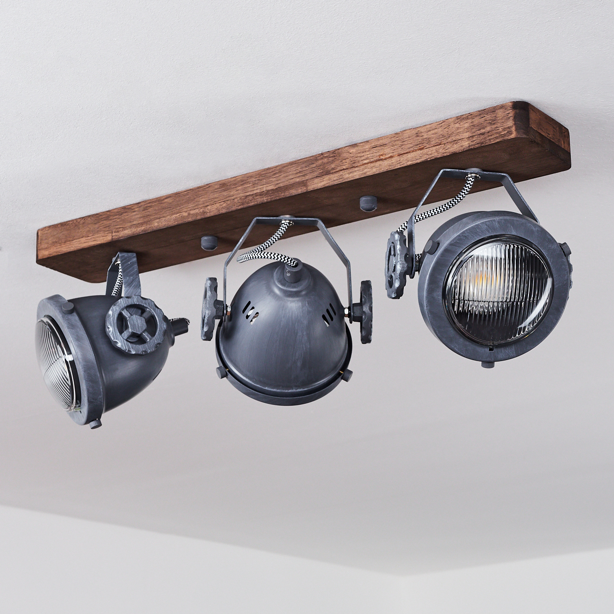 Drei graue Industriascheinwerfer auf einem rustikalen Holzbalken an weißer Decke montiert.