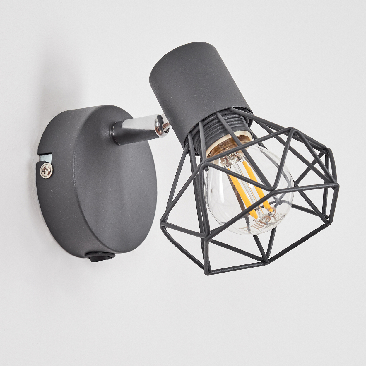 Eine moderne graue Wandleuchte mit einem schwarzen geometrischen Käfig um eine klare Edison-Glühbirne.