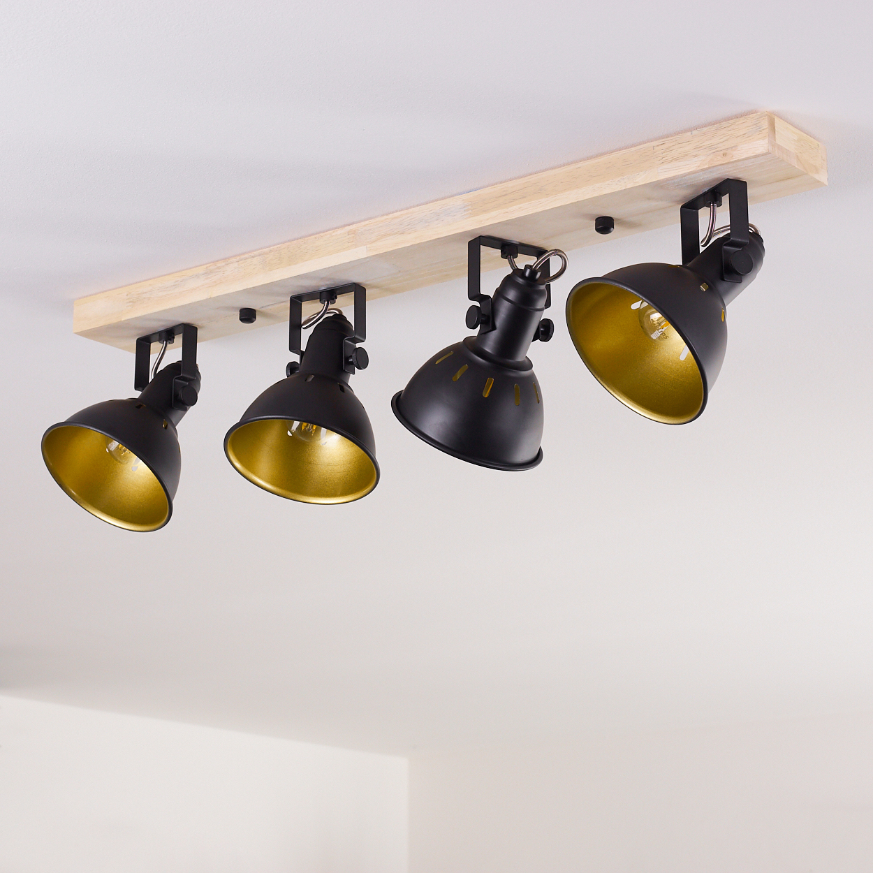 Vier schwarze Lampenschirme mit goldener Innenseite auf einer Holzleiste.