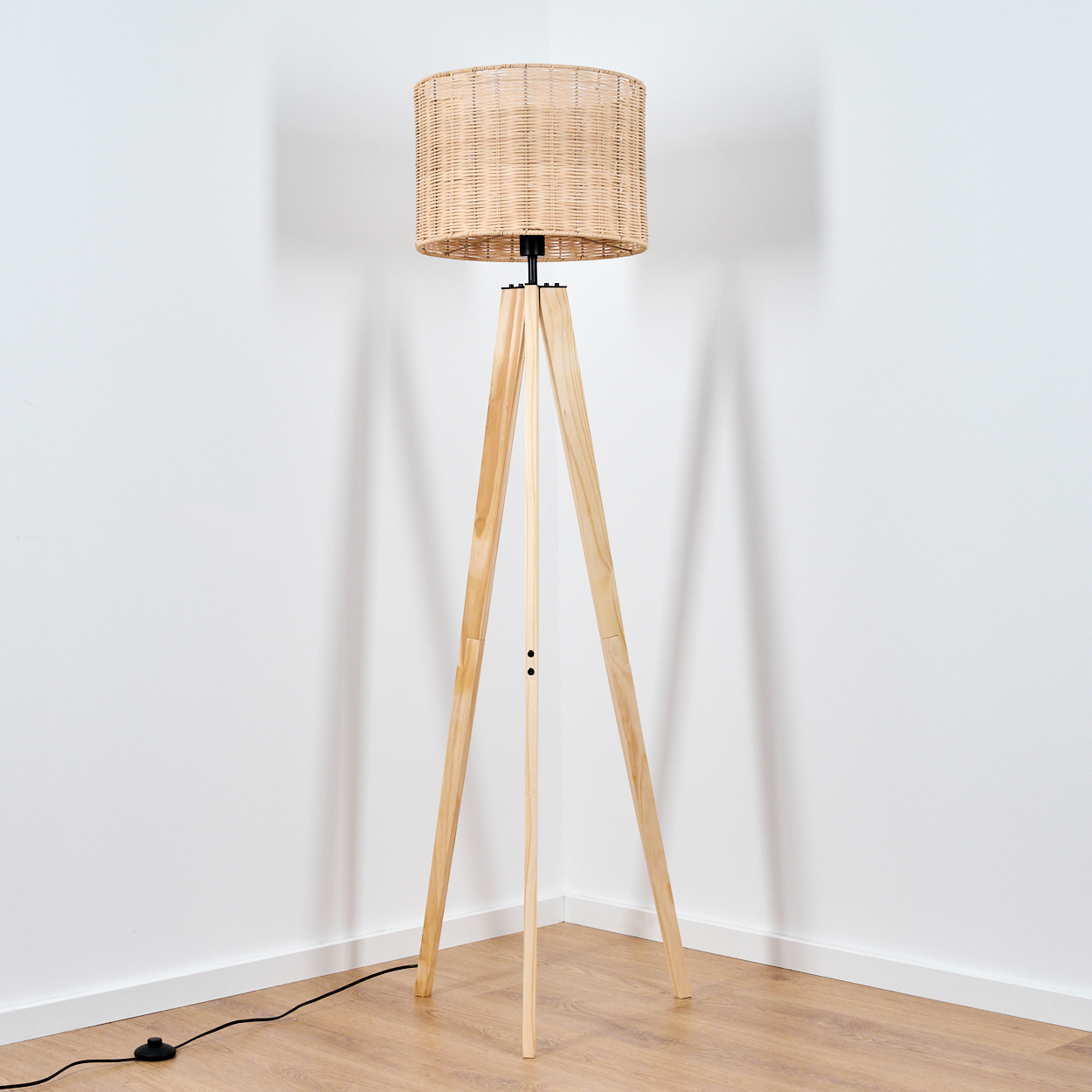 Eine Stehlampe mit gewebtem Schirm und dreibeinigem Holzgestell steht in einer Ecke.