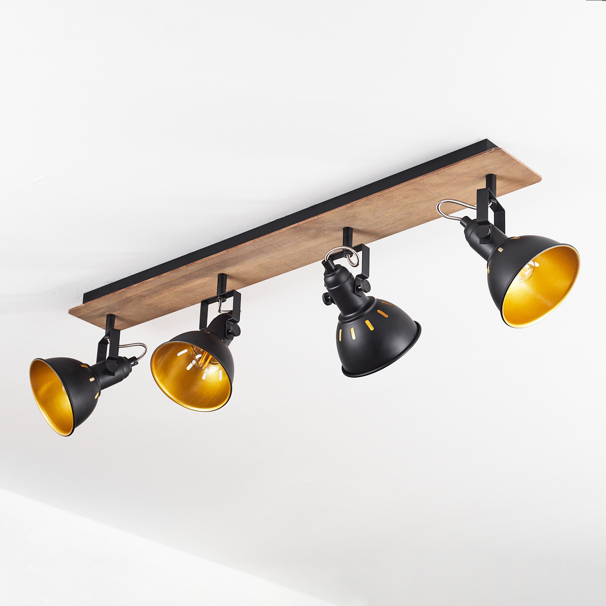 Vier schwarze Deckenstrahler mit goldener Innenseite auf Holzsockel an weißer Decke.