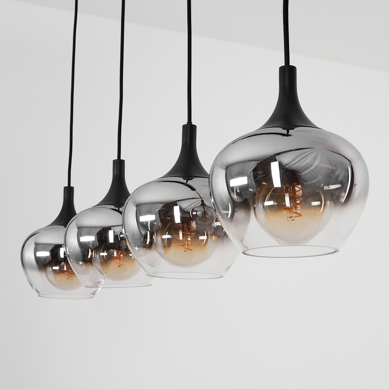 Vier Pendelleuchten mit rauchigem Glas und sichtbaren Glühbirnen.