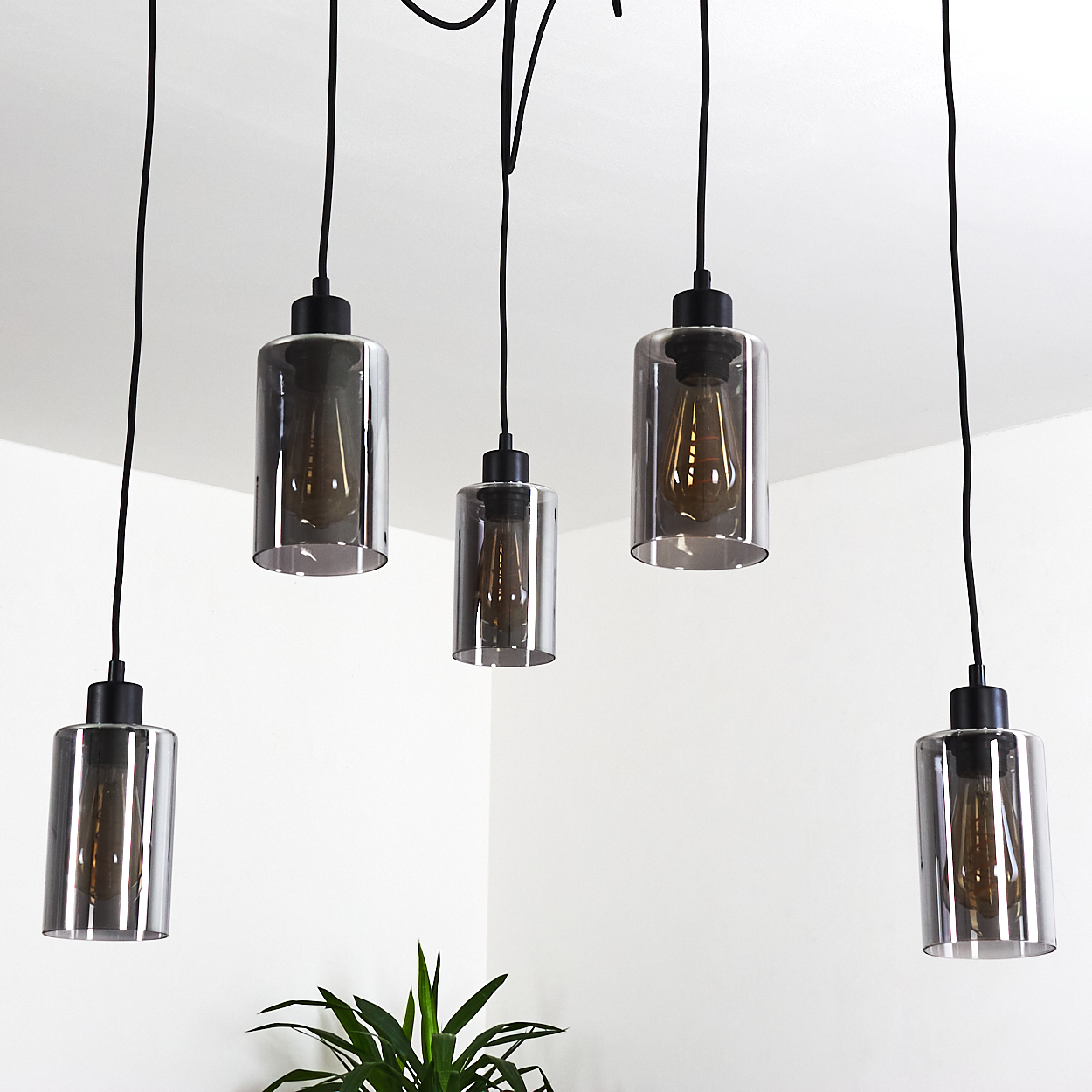 Fünf Pendelleuchten mit rauchglaszylindern und sichtbaren Edison-Glühbirnen hängen von schwarzen Kabeln.