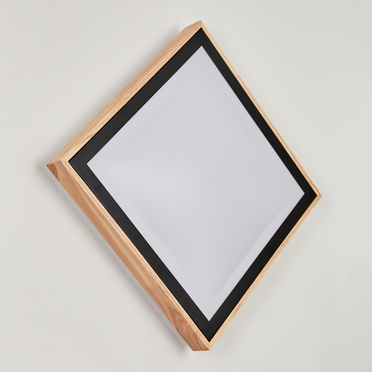 Ein rautenförmiger Spiegel mit Holzrahmen und schwarzer Kante an einer weißen Wand.